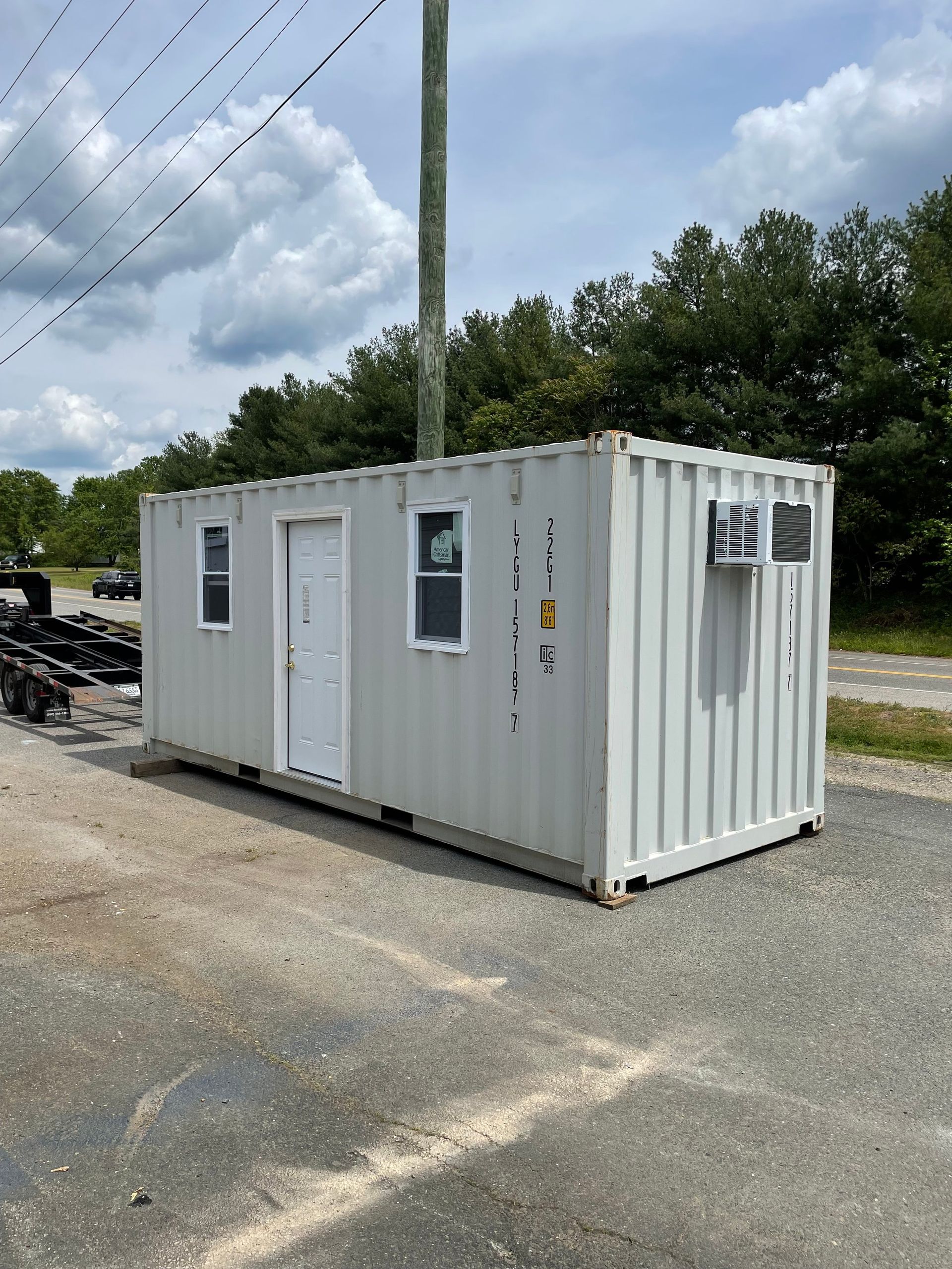 A white shipping container with a door and windows is parked on the side of the road.