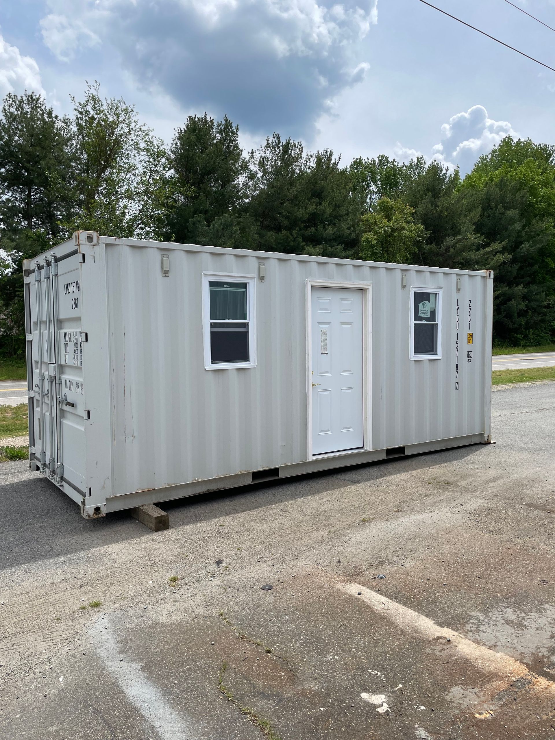 A shipping container with a door and two windows is parked in a parking lot.