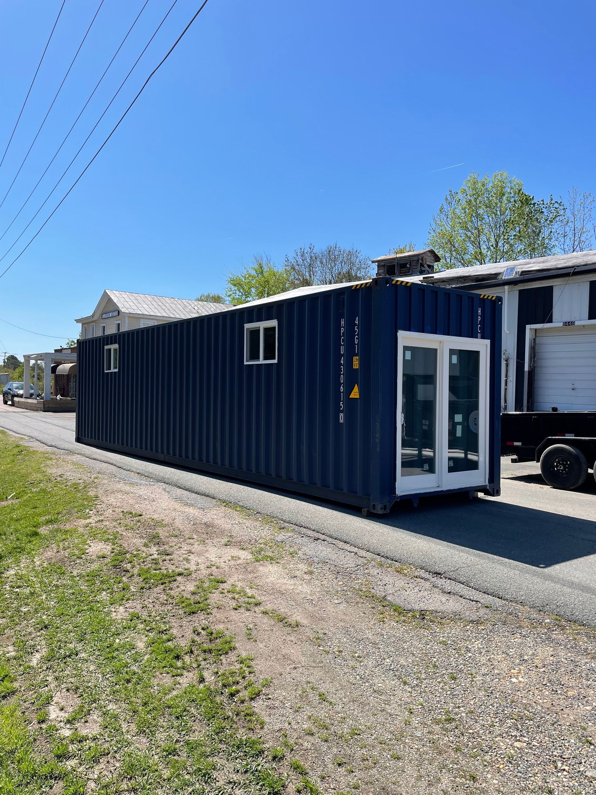 A blue shipping container with white windows and doors is parked on the side of the road.
