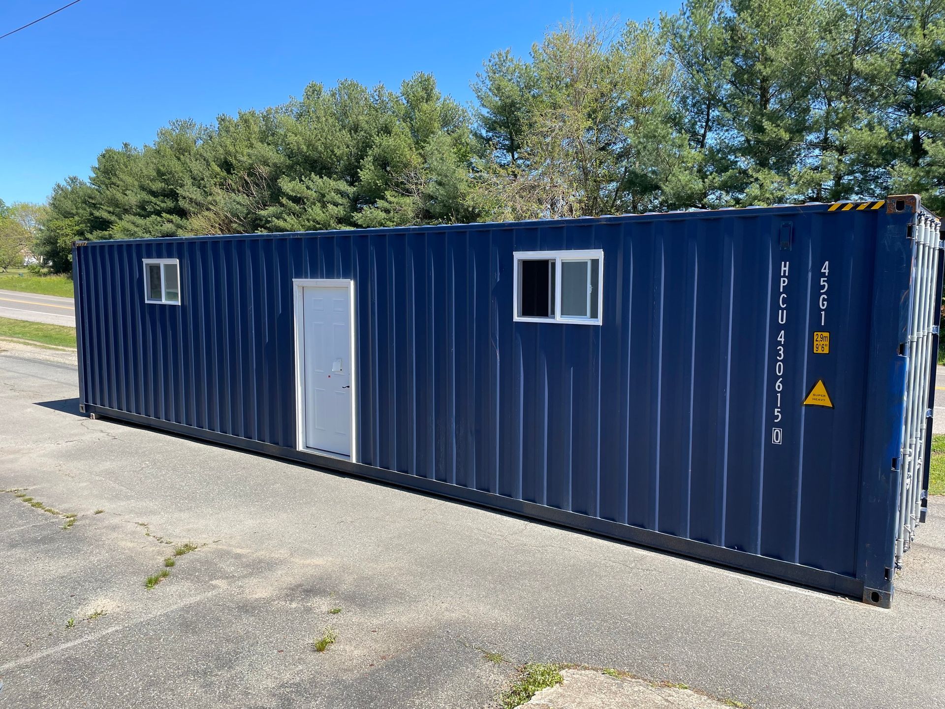 A blue shipping container with two windows and a door is parked on the side of the road.