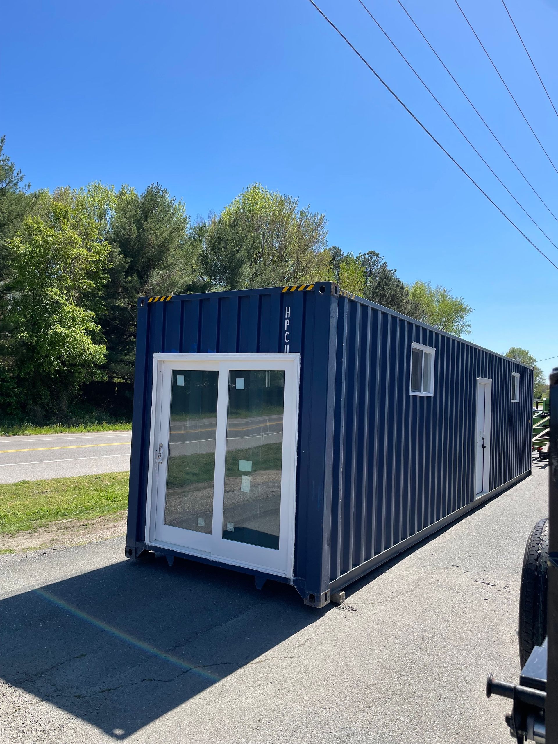 A blue shipping container with white windows is parked on the side of the road.