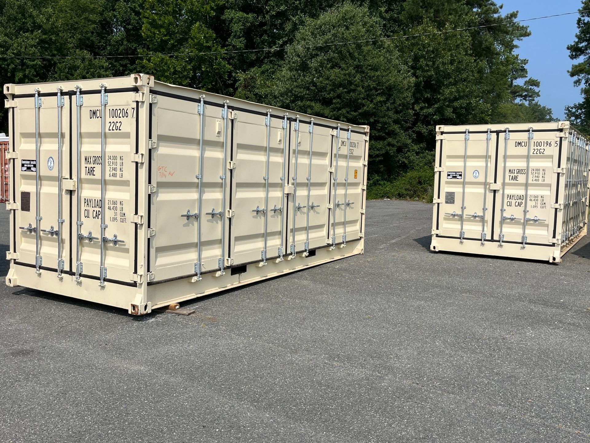 Two shipping containers are parked next to each other on a gravel road.
