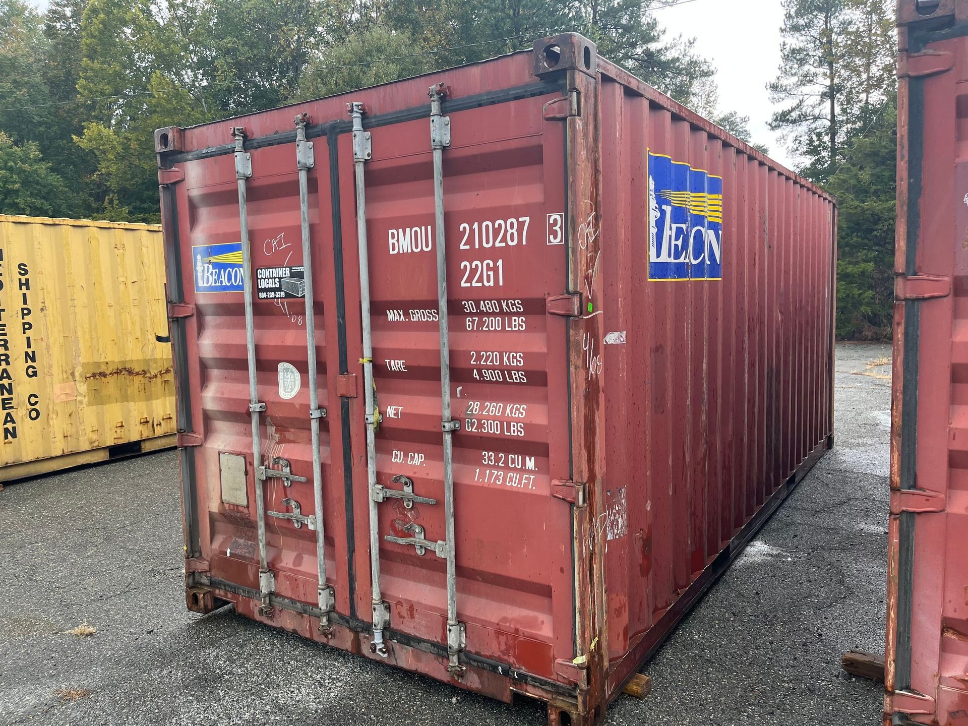 A red shipping container is parked in a gravel lot.