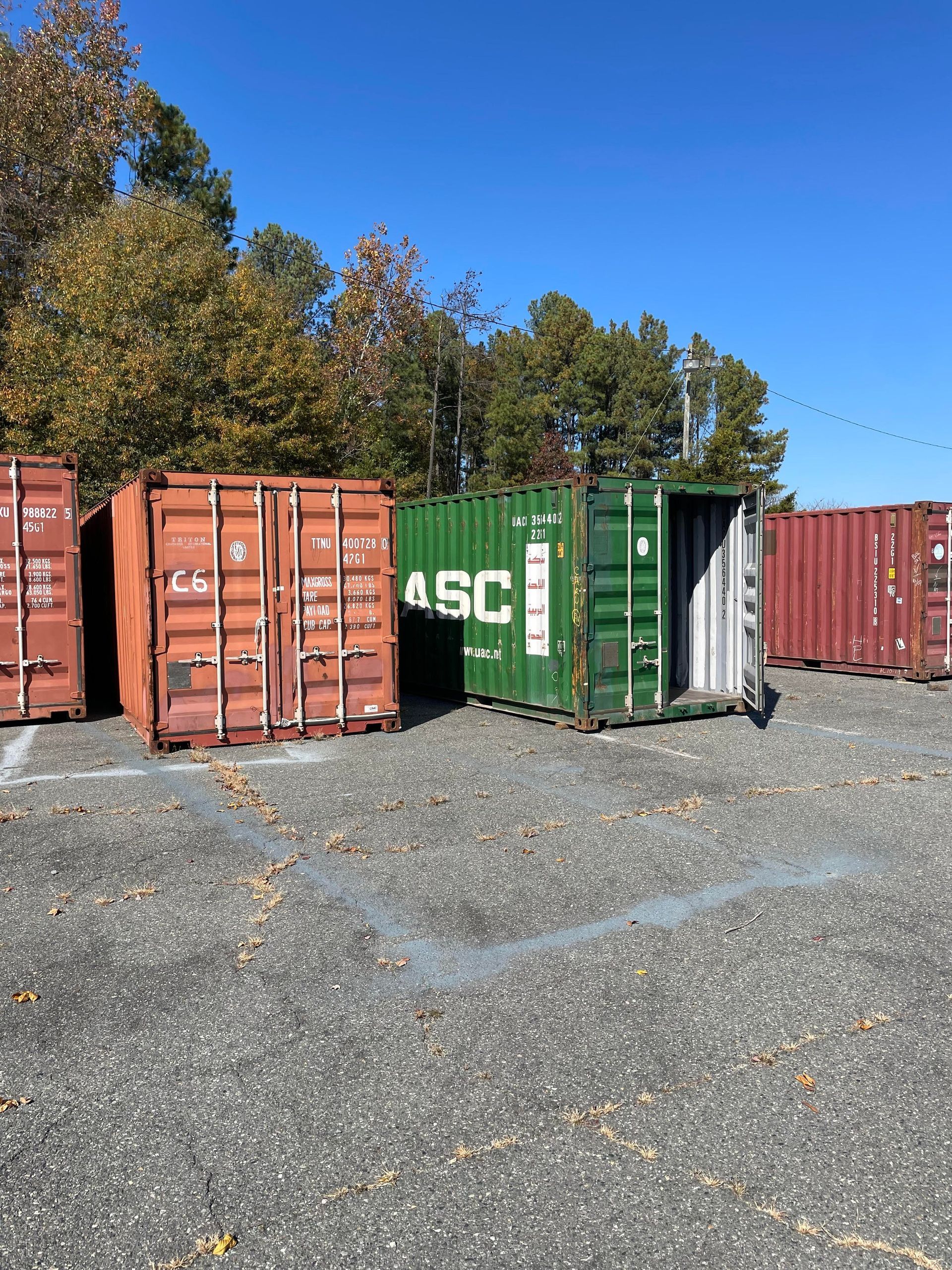 A row of shipping containers are lined up in a gravel lot.