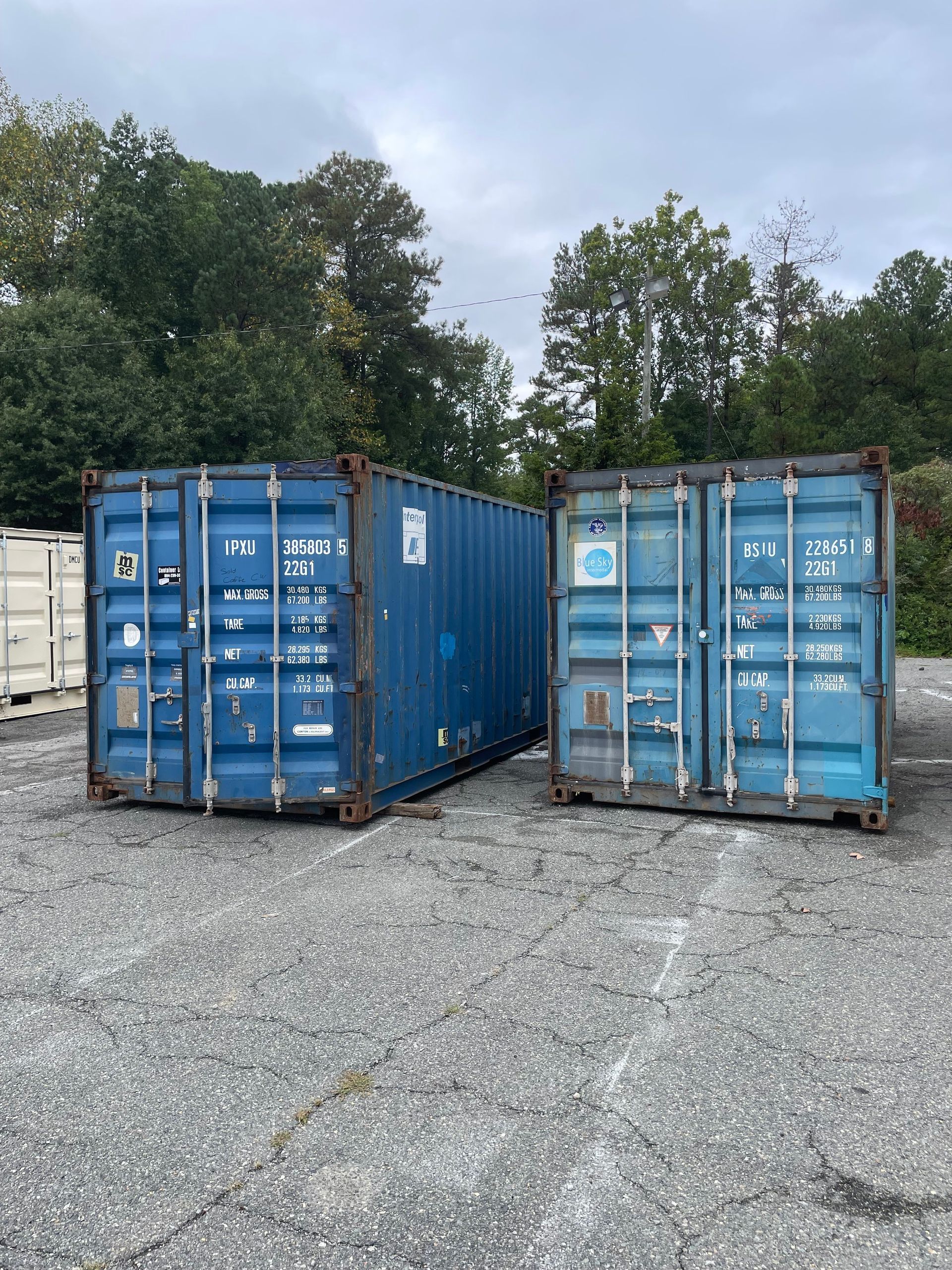 Two blue shipping containers are sitting next to each other in a gravel lot.