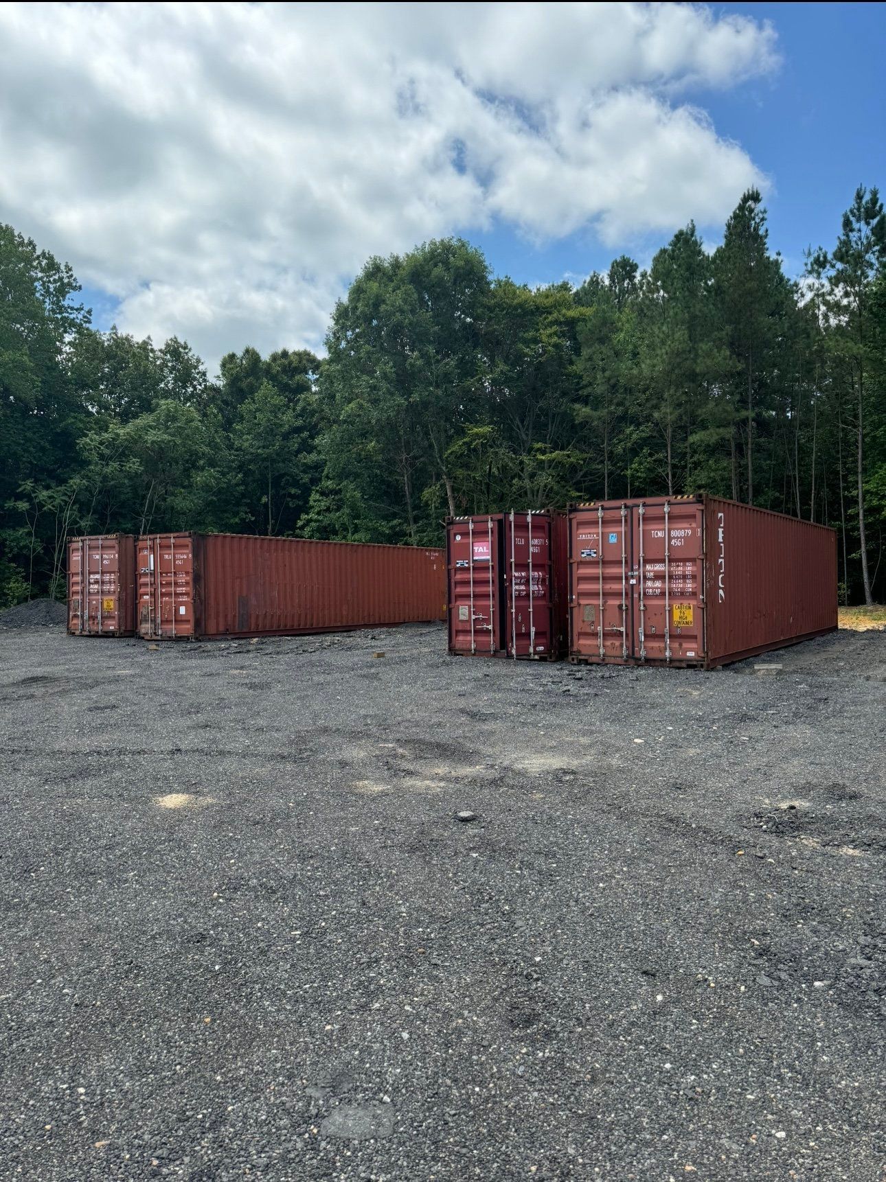 A row of red shipping containers are sitting in a gravel lot.