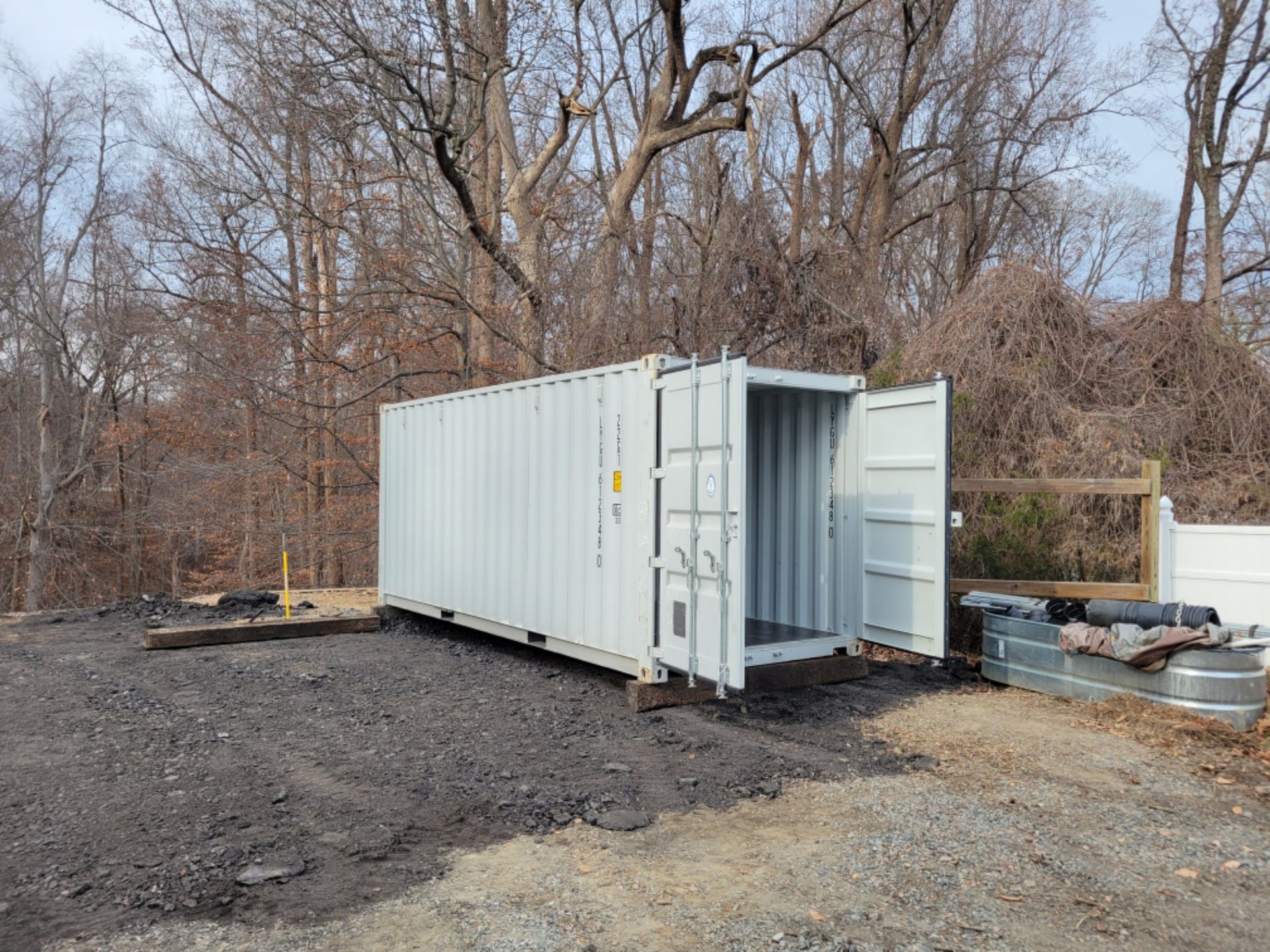 A white shipping container is sitting in a dirt lot with its door open.