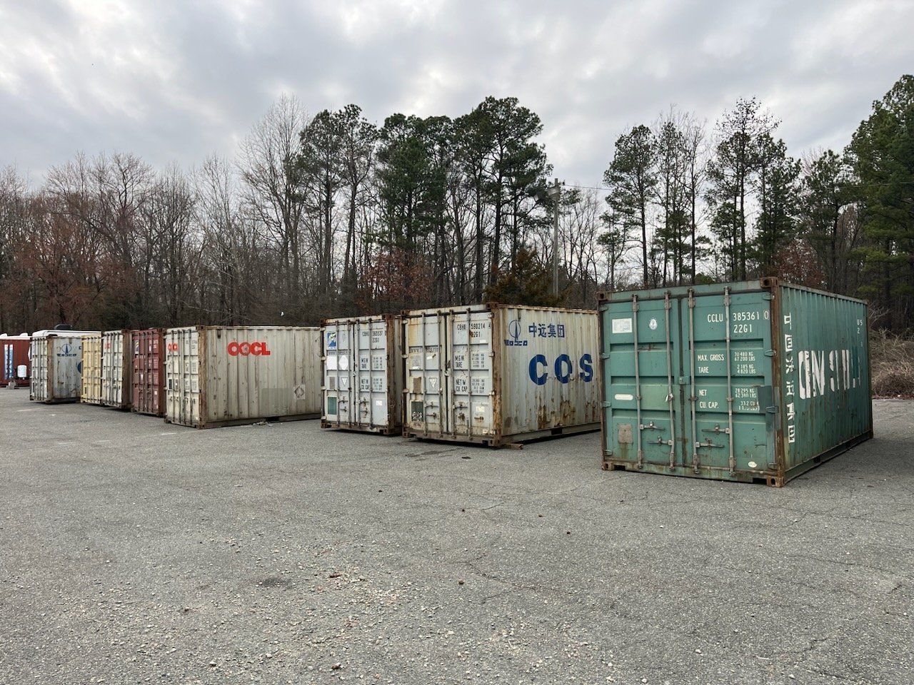 A row of shipping containers are lined up in a gravel lot.