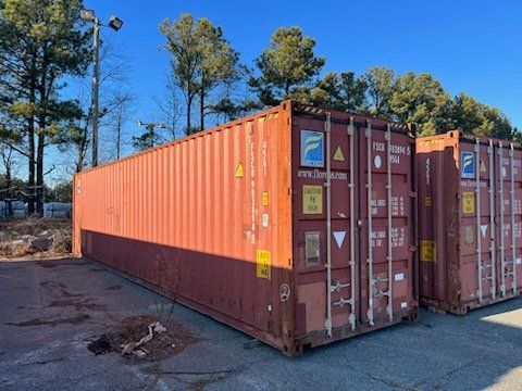 A row of red shipping containers are lined up in a parking lot.