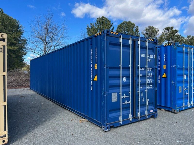 A row of blue shipping containers are parked in a parking lot