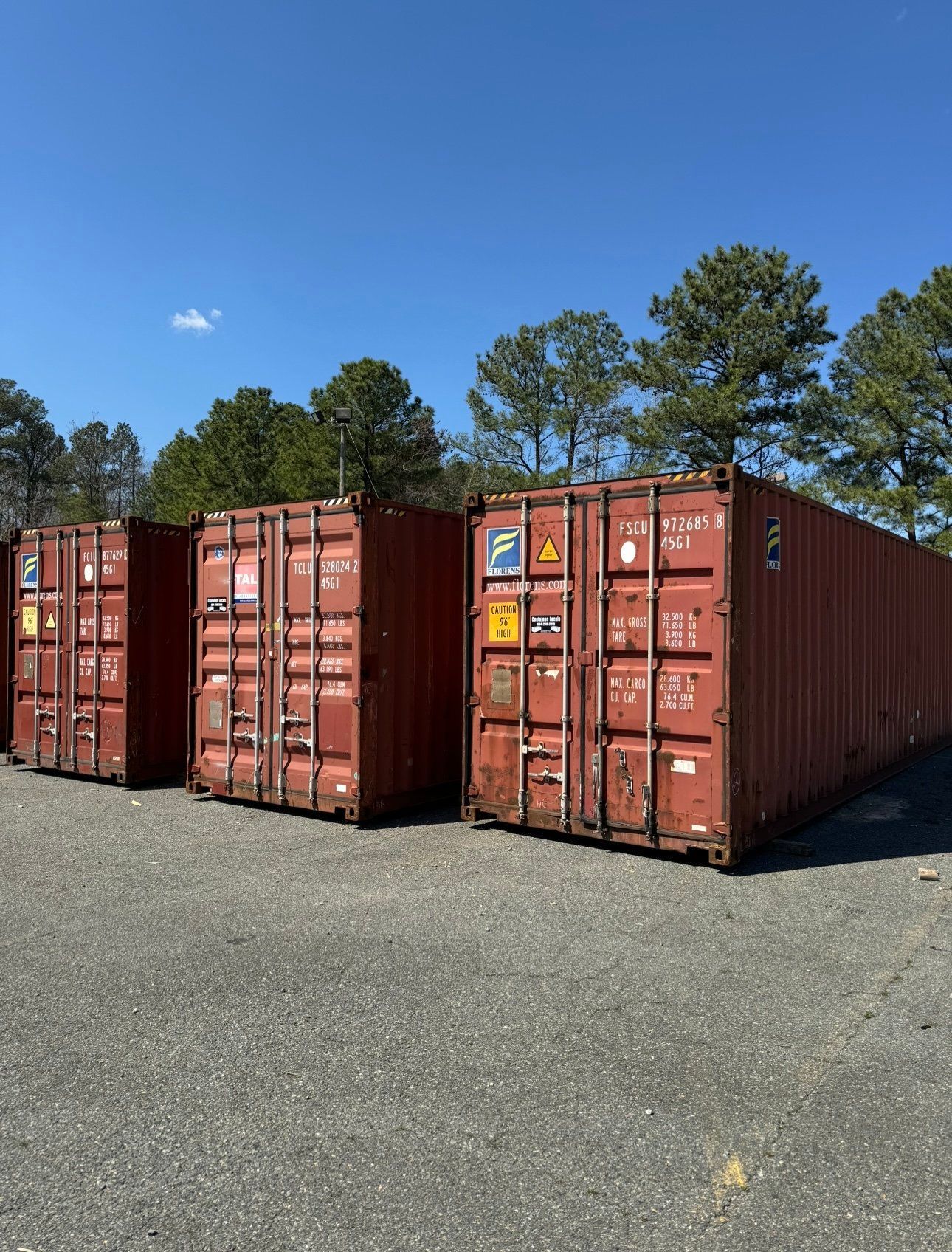 A row of red shipping containers are lined up in a parking lot.