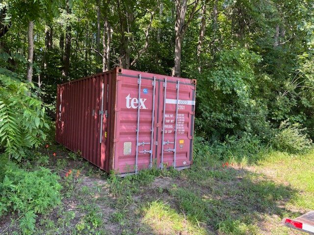 A red shipping container is sitting in the middle of a forest.