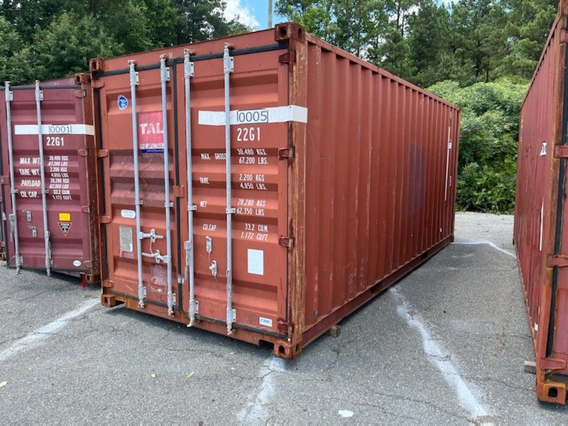 A row of red shipping containers are parked in a parking lot.
