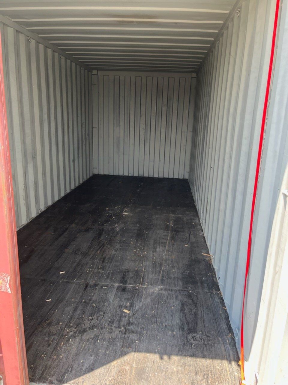 An empty shipping container with a black floor and a red door.