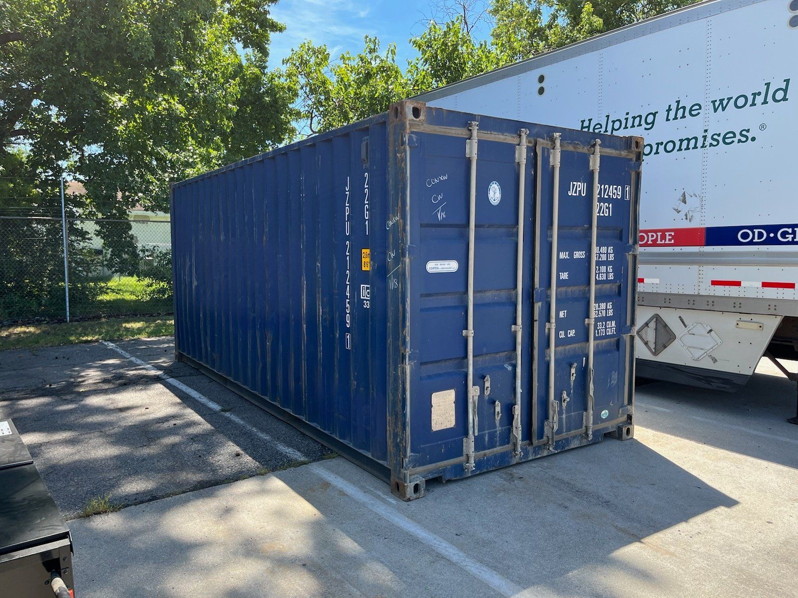 A blue shipping container is parked in a parking lot next to a white truck.
