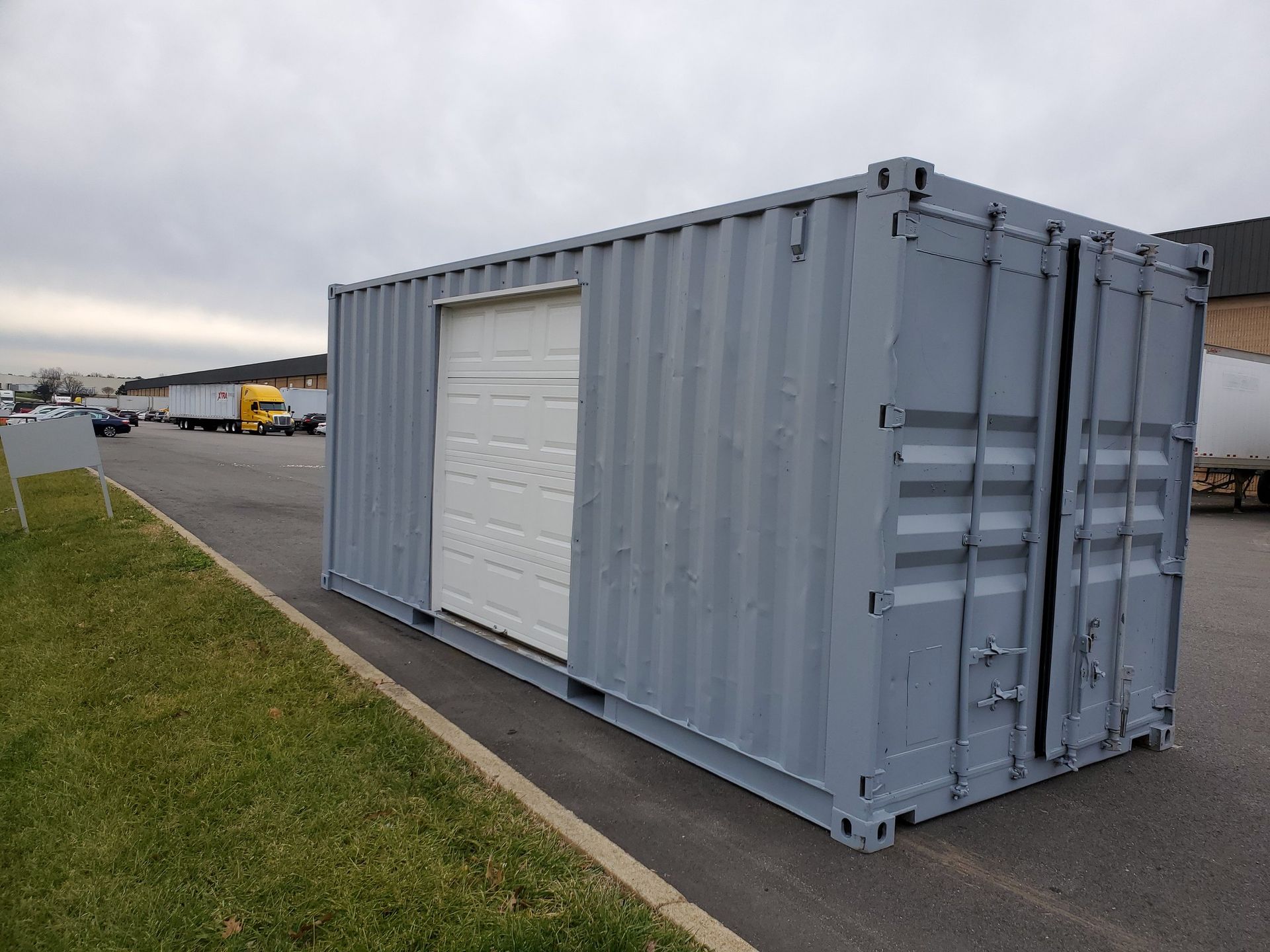 A shipping container with a garage door is sitting in a parking lot.