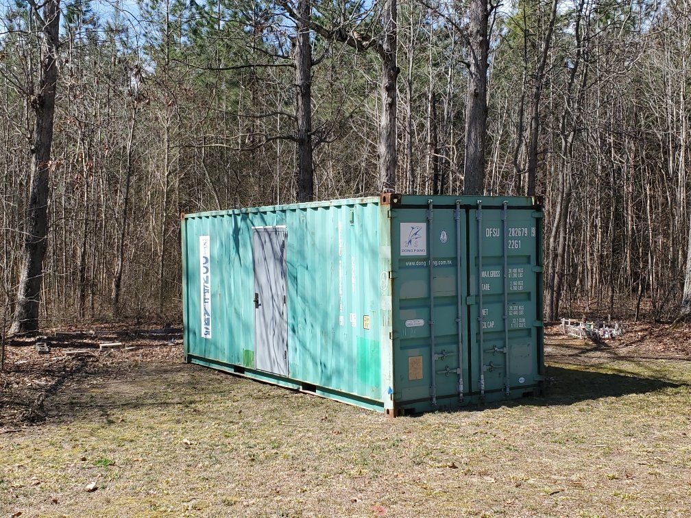 A green shipping container is sitting in a grassy field in the middle of a forest.