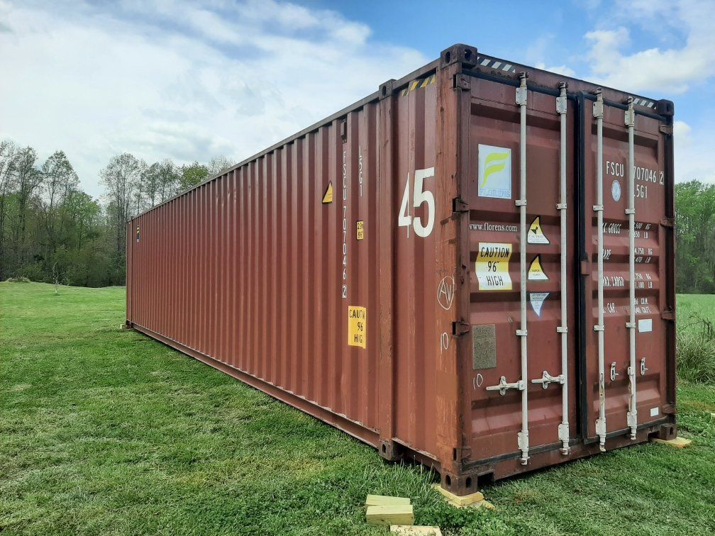 A large red shipping container is sitting in the middle of a grassy field.