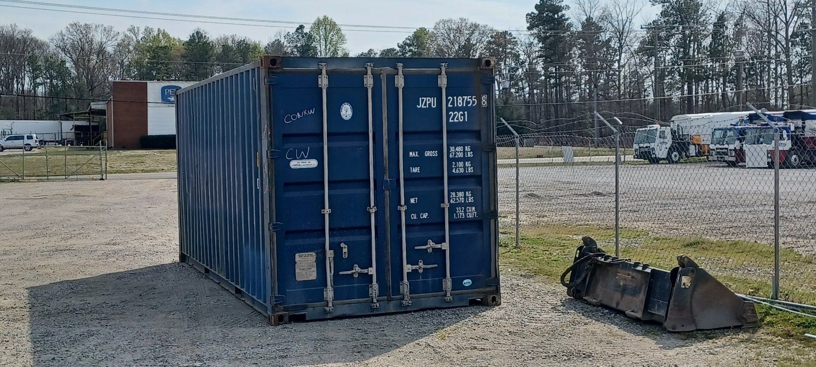 A blue shipping container is sitting in the middle of a gravel lot.