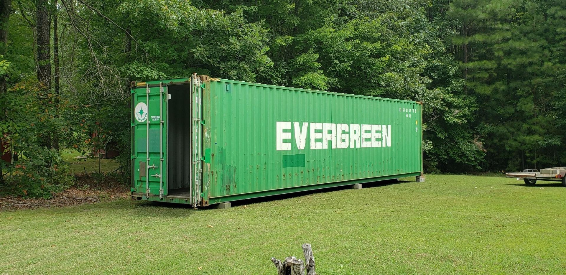 A green evergreen shipping container is sitting in a grassy field.