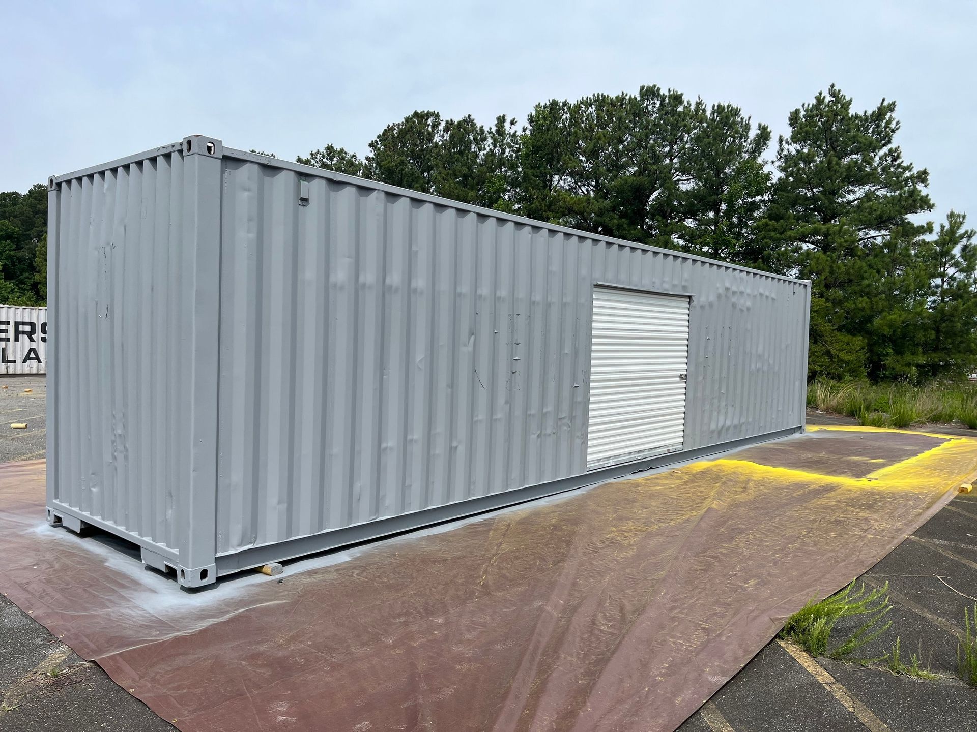 A large gray shipping container with a white door is sitting on top of a red mat.