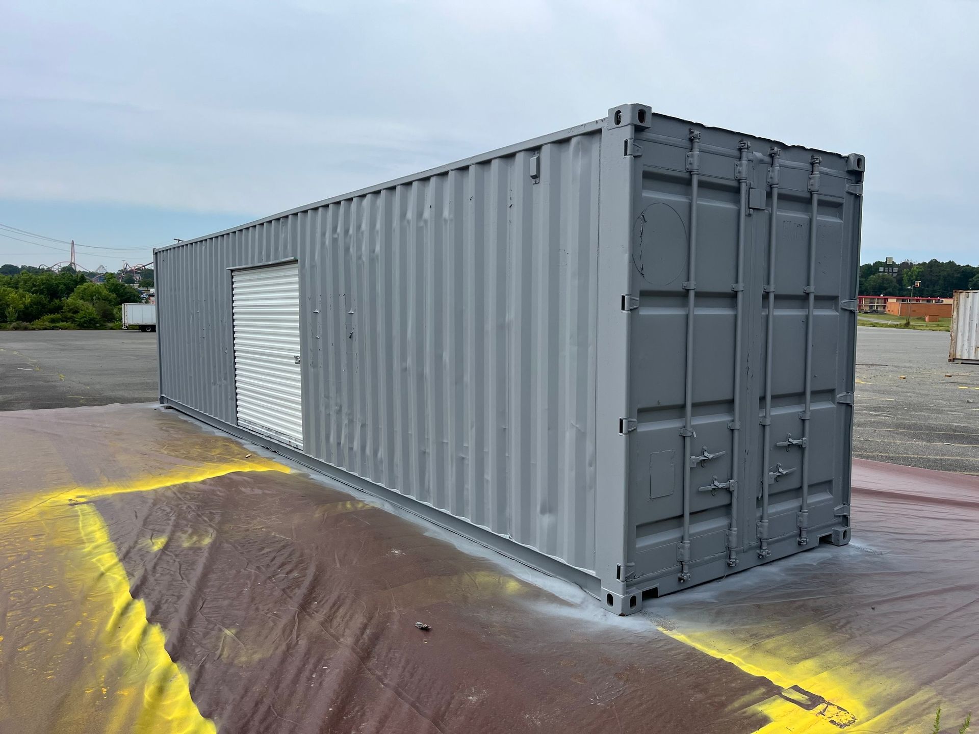 A gray shipping container with a white door is sitting in a parking lot.