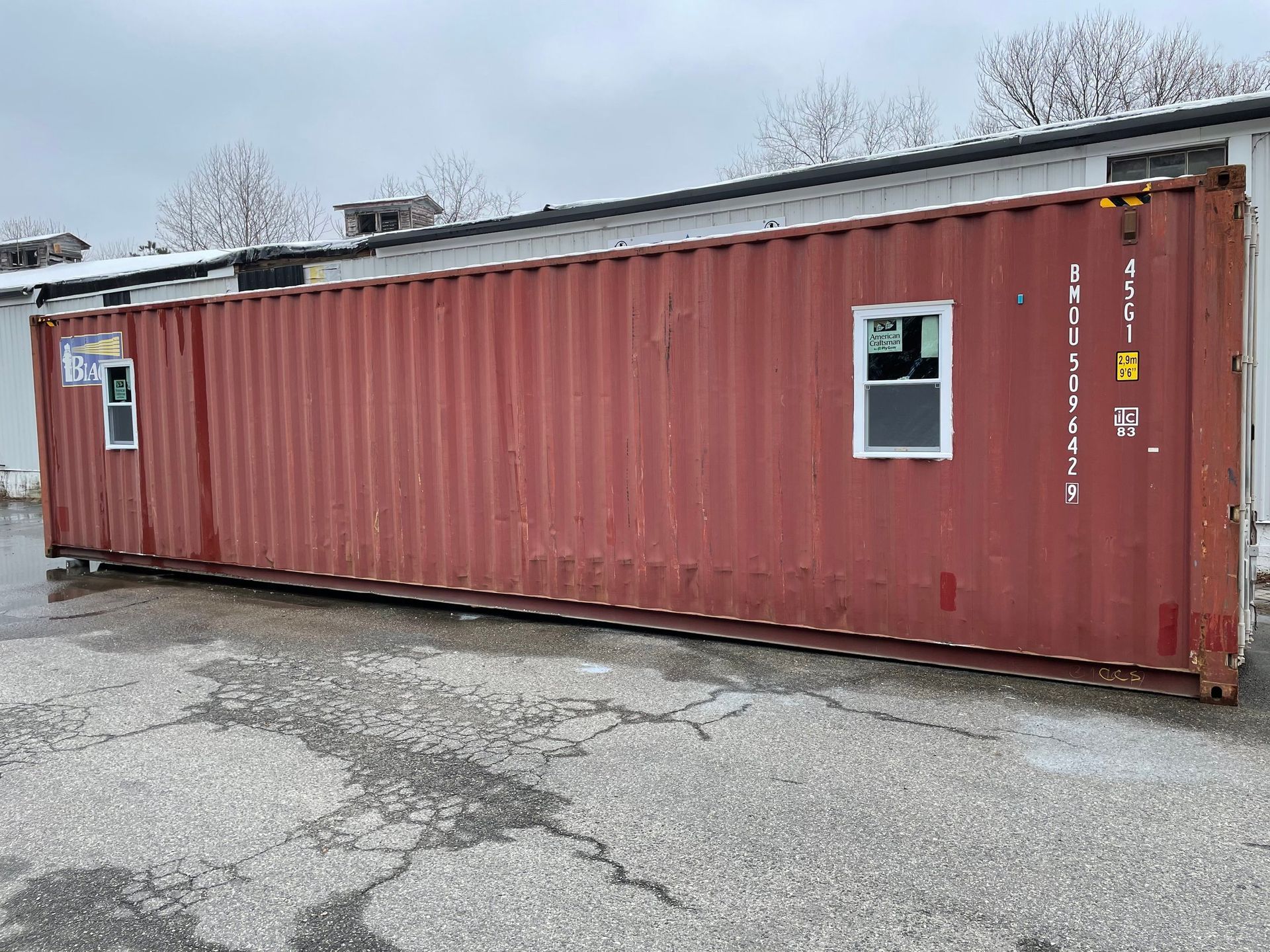 A red shipping container with two windows is parked in front of a building.