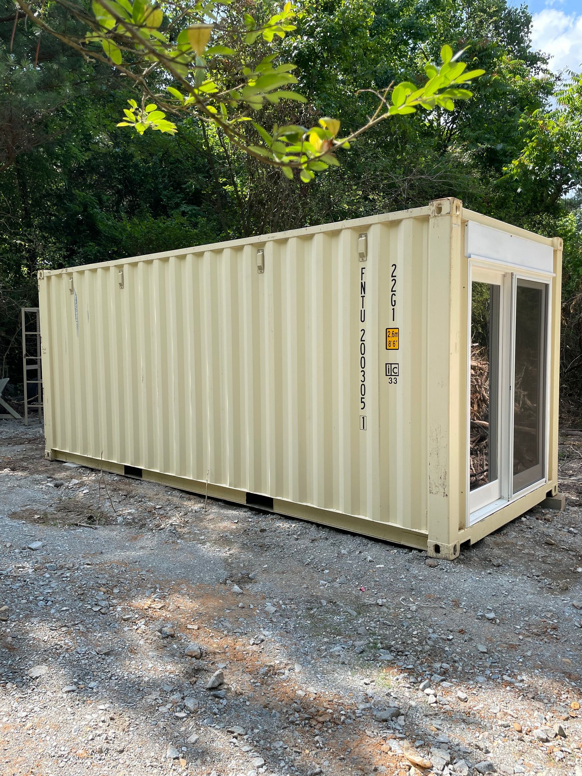 A shipping container with a glass door is sitting on top of a gravel road.