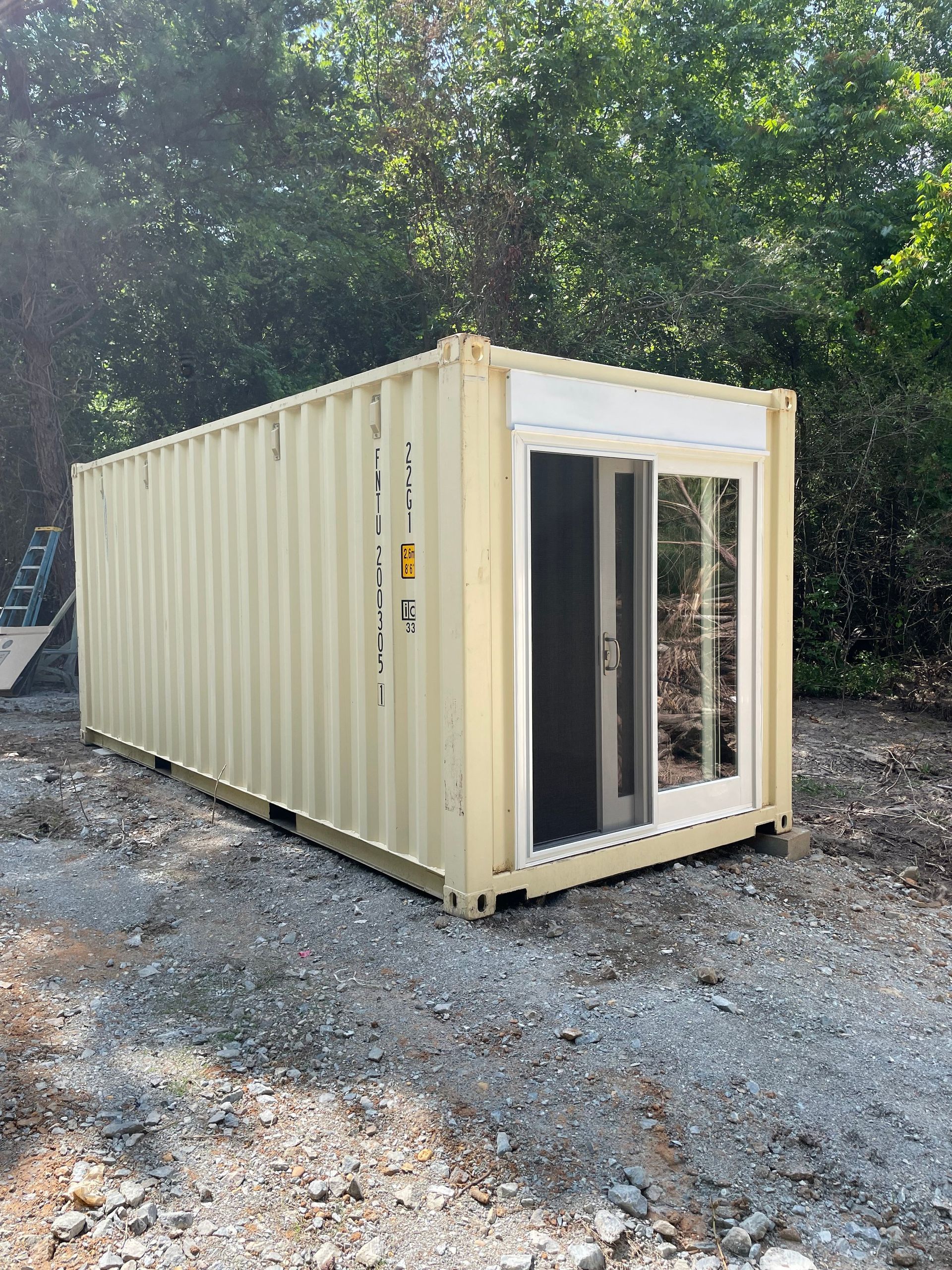 A shipping container with a sliding glass door is sitting in a gravel lot.
