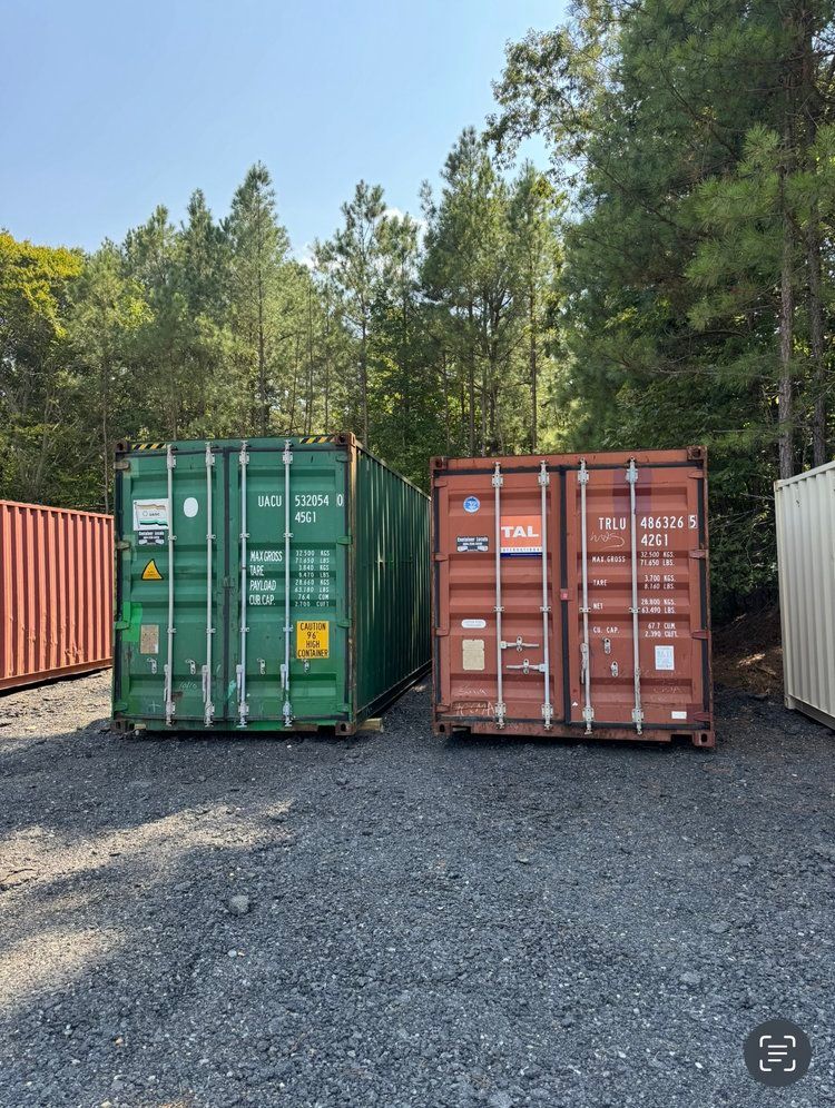 Two shipping containers are parked next to each other in a gravel lot.