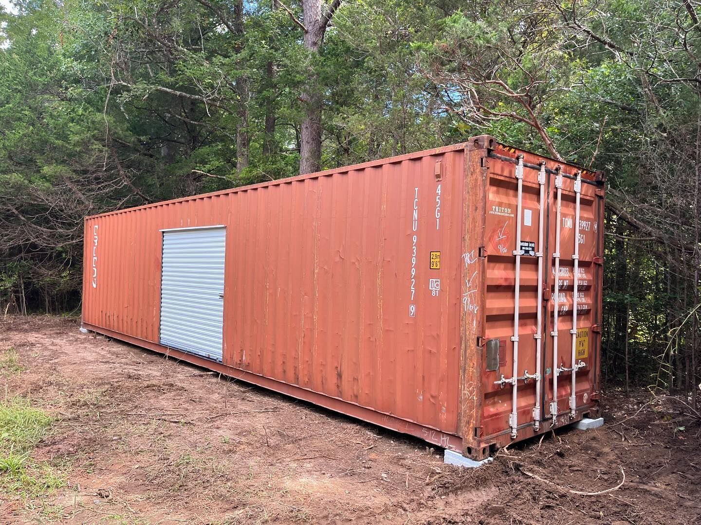 A red shipping container with a garage door is sitting in the middle of a field.