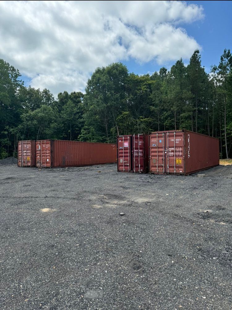 A row of red shipping containers are sitting in a gravel lot.