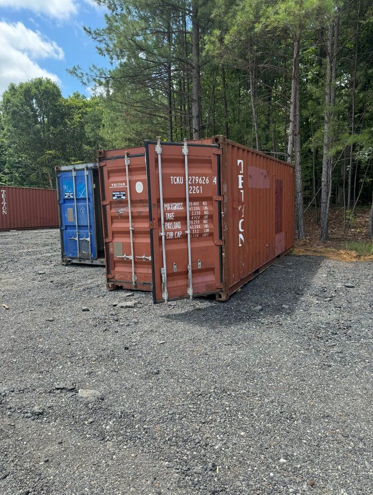 A row of shipping containers are parked in a gravel lot.