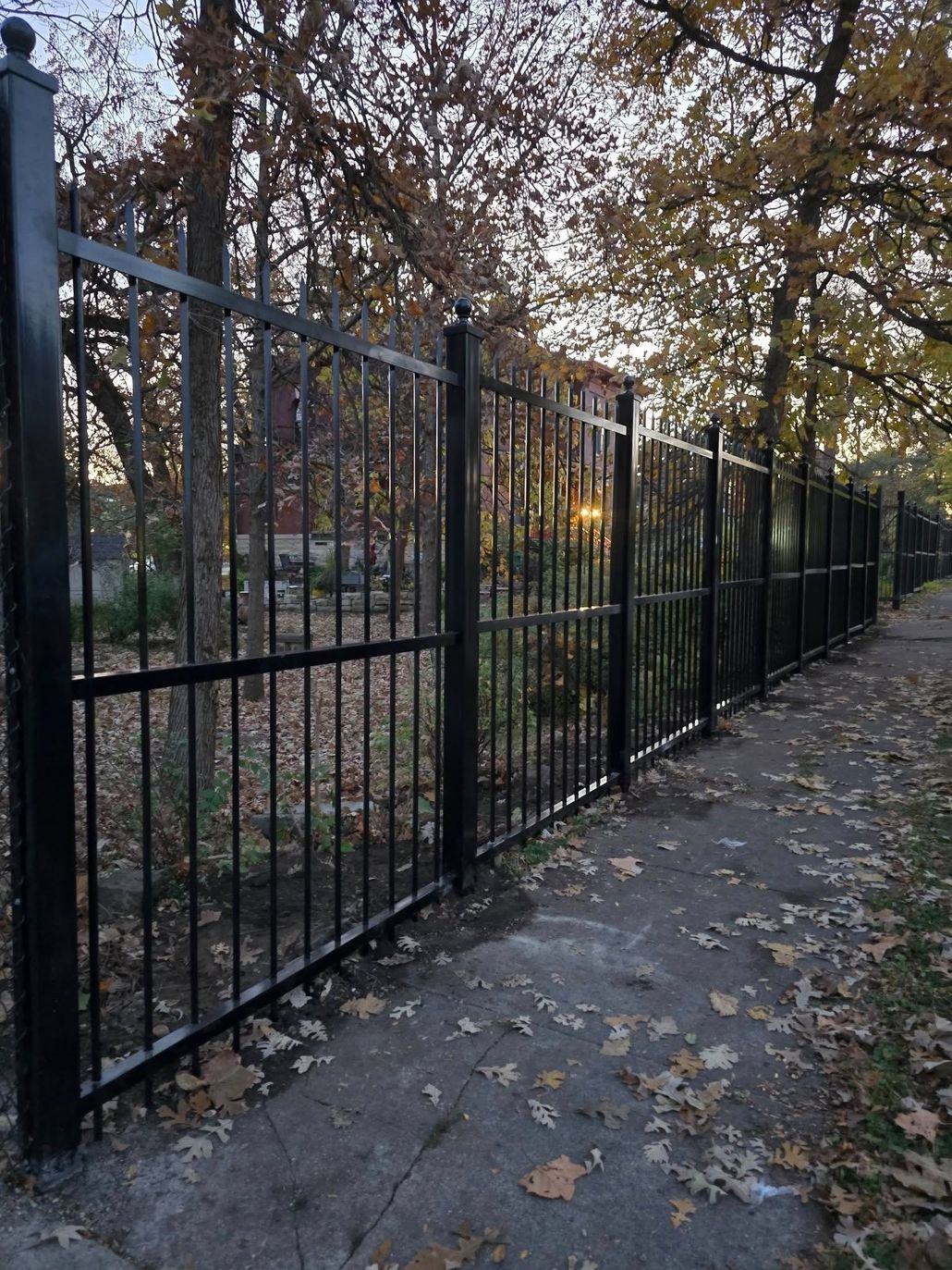 Gated driveway leading to a large white mansion with manicured gardens and stone pillars