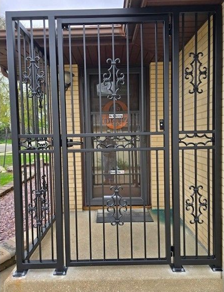 Black metal security gate with decorative scrollwork in a doorway, viewed from the outside.