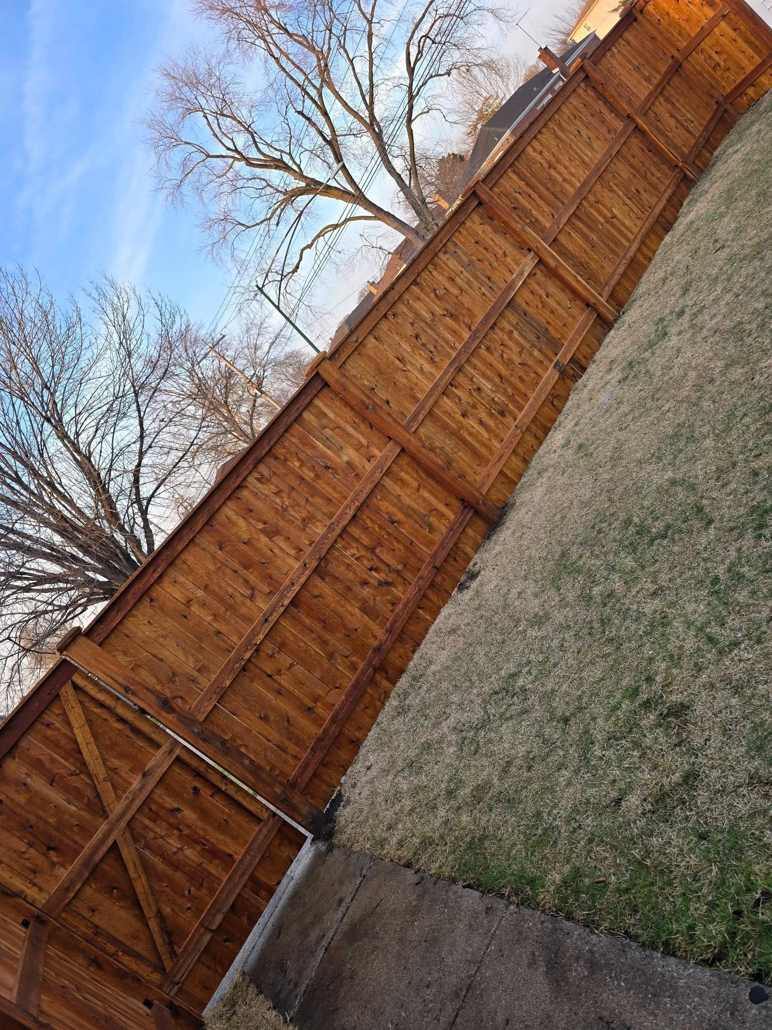 Wooden backyard fence beside a grass lawn and concrete path under a clear blue sky