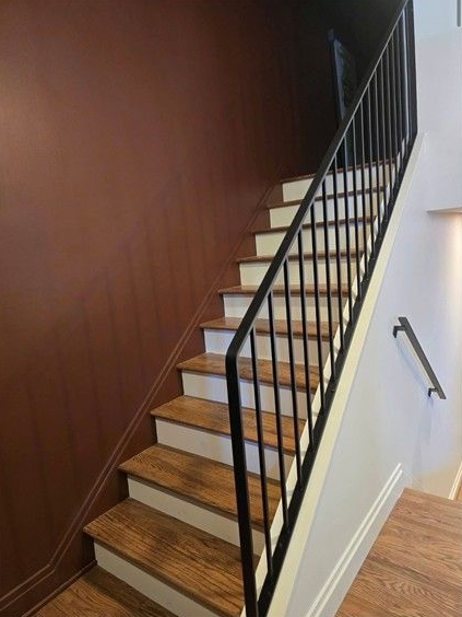 Indoor staircase with wood steps, black railing, and white walls beside a brown accent wall