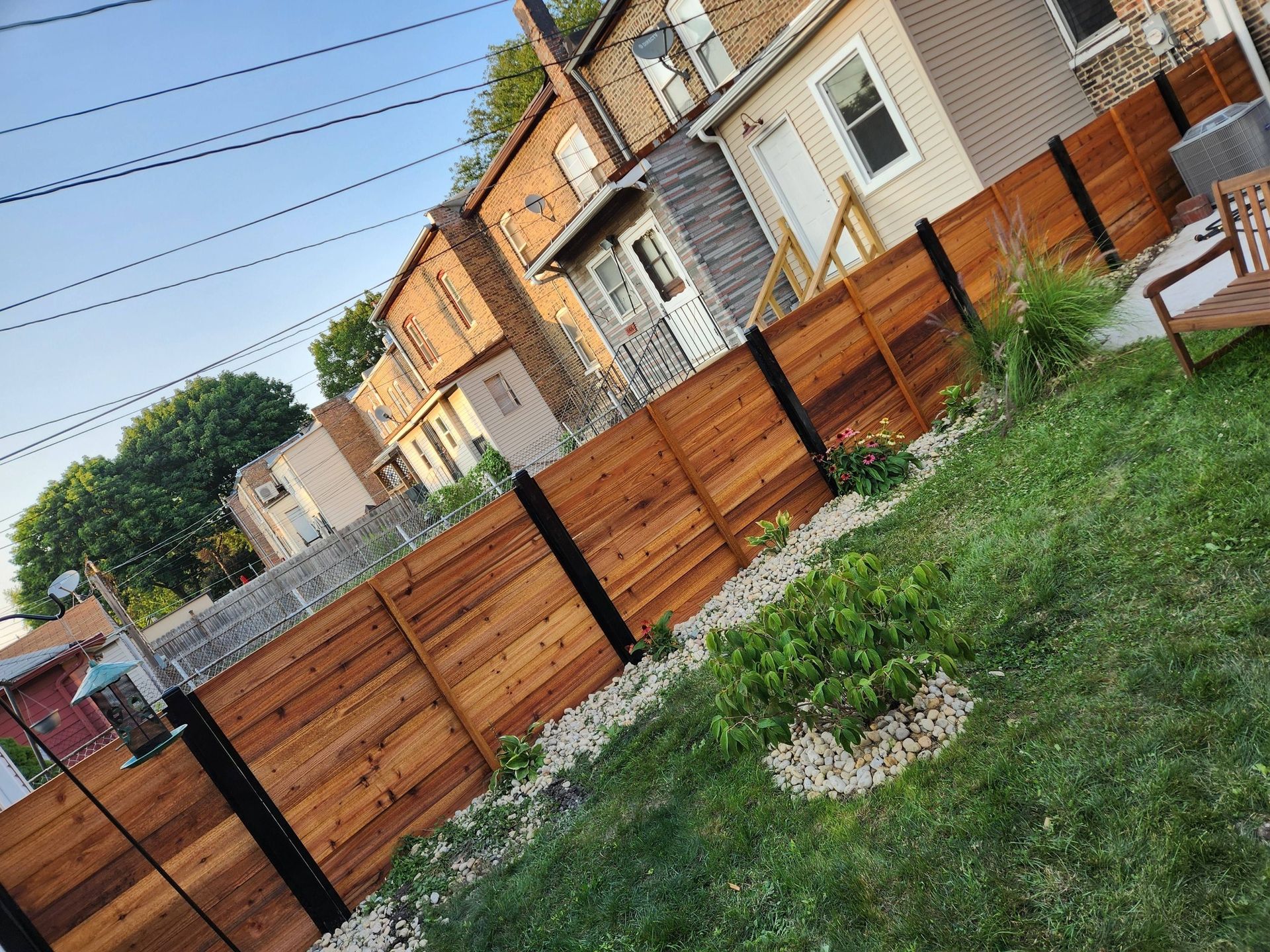 Tilted view of a grassy backyard with a wooden fence and row of houses beyond