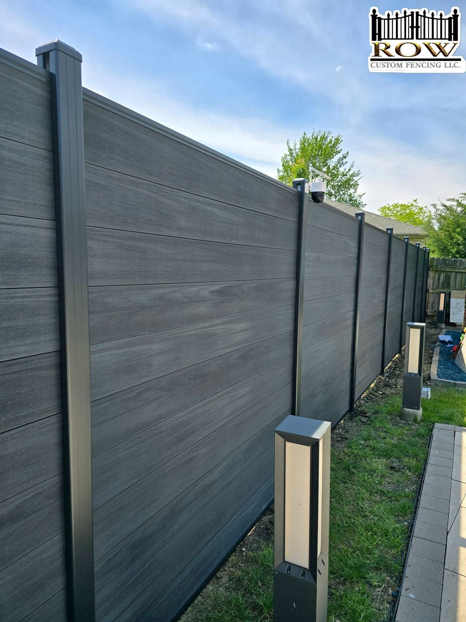 Dark wood privacy fence with gray posts beside a gravel path and solar lights in a landscaped yard