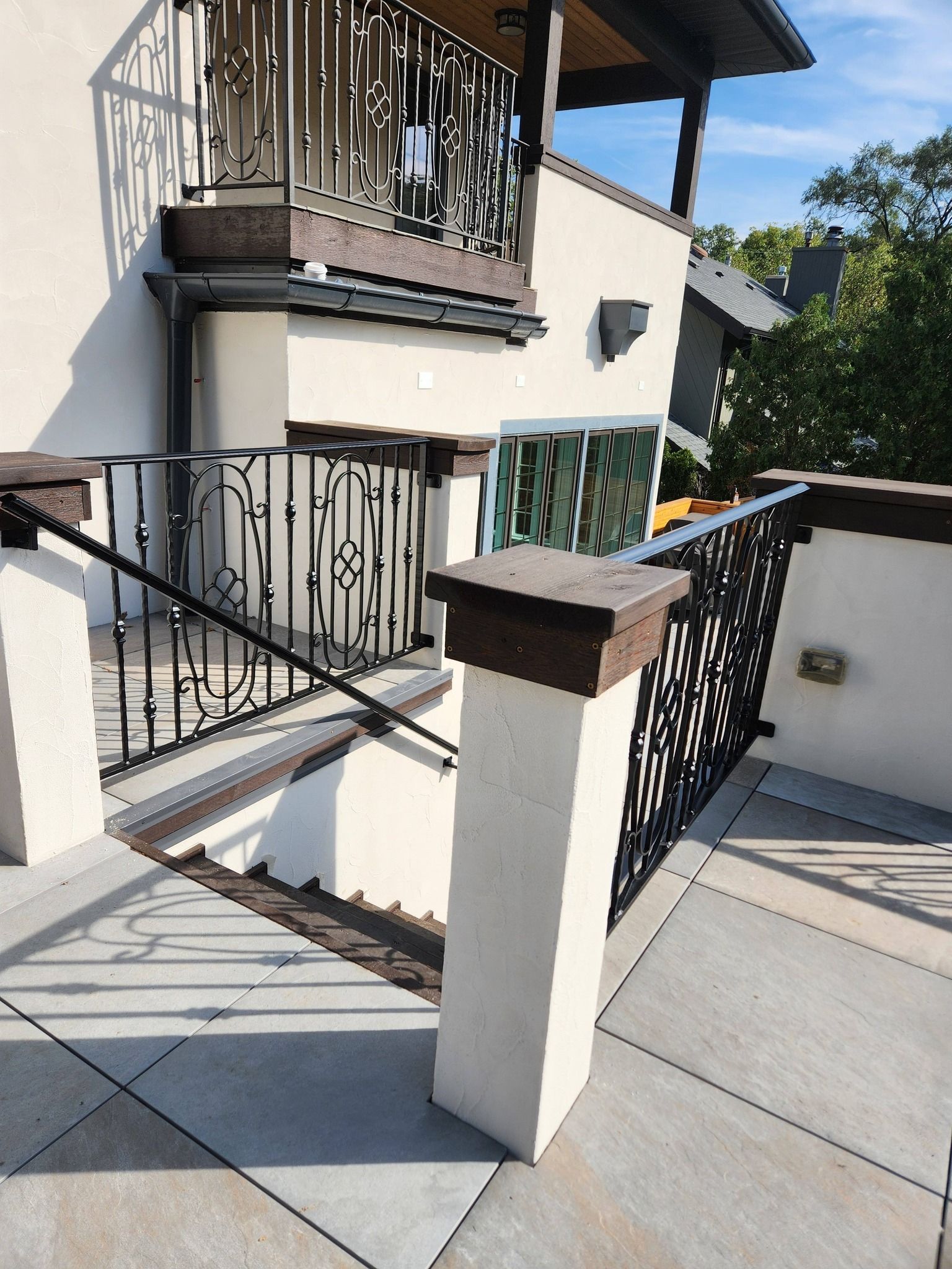 Outdoor staircase with black wrought-iron railings beside a cream stucco building and balcony