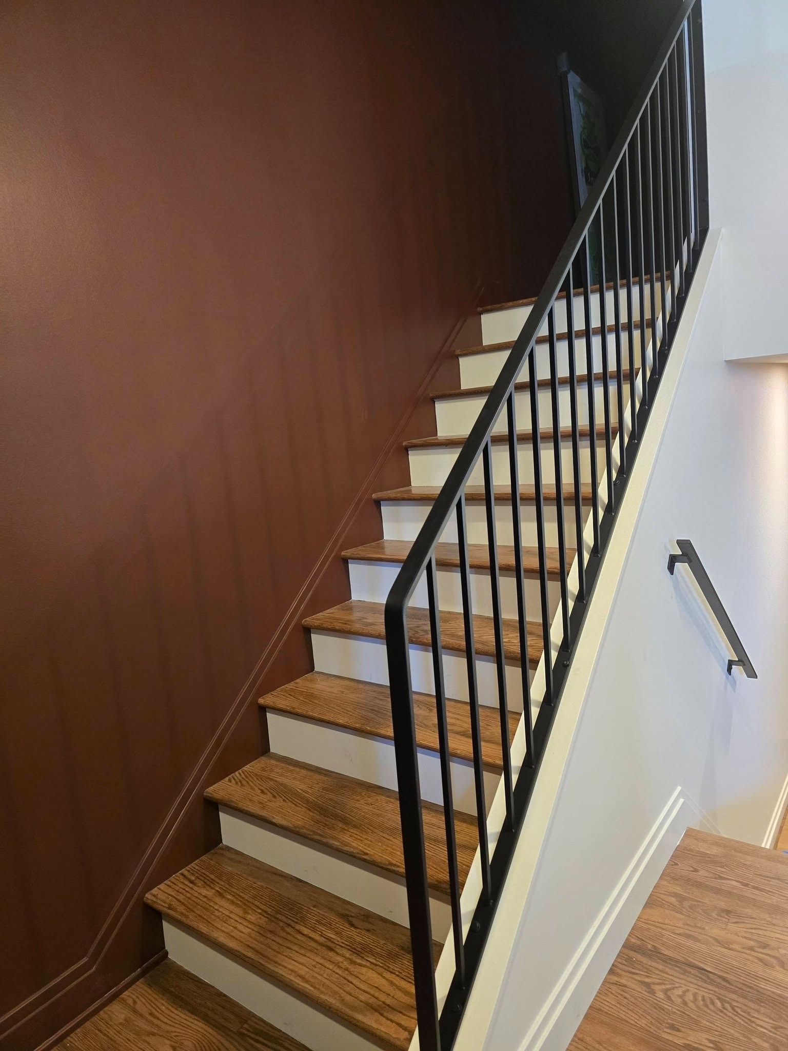 Interior staircase with wooden steps, black railings, and brown and white walls