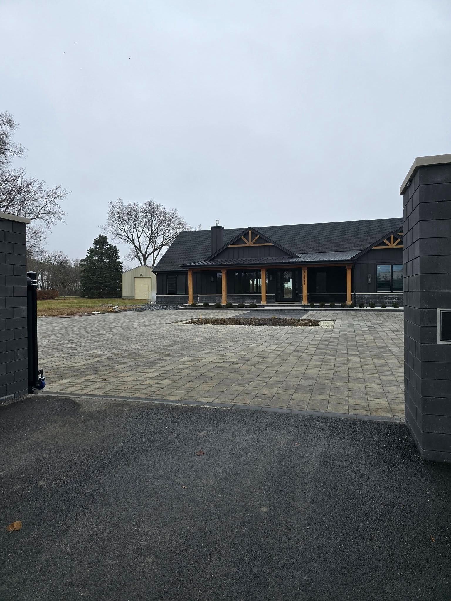 Gravel driveway leading to a large dark house with a covered porch on an overcast day