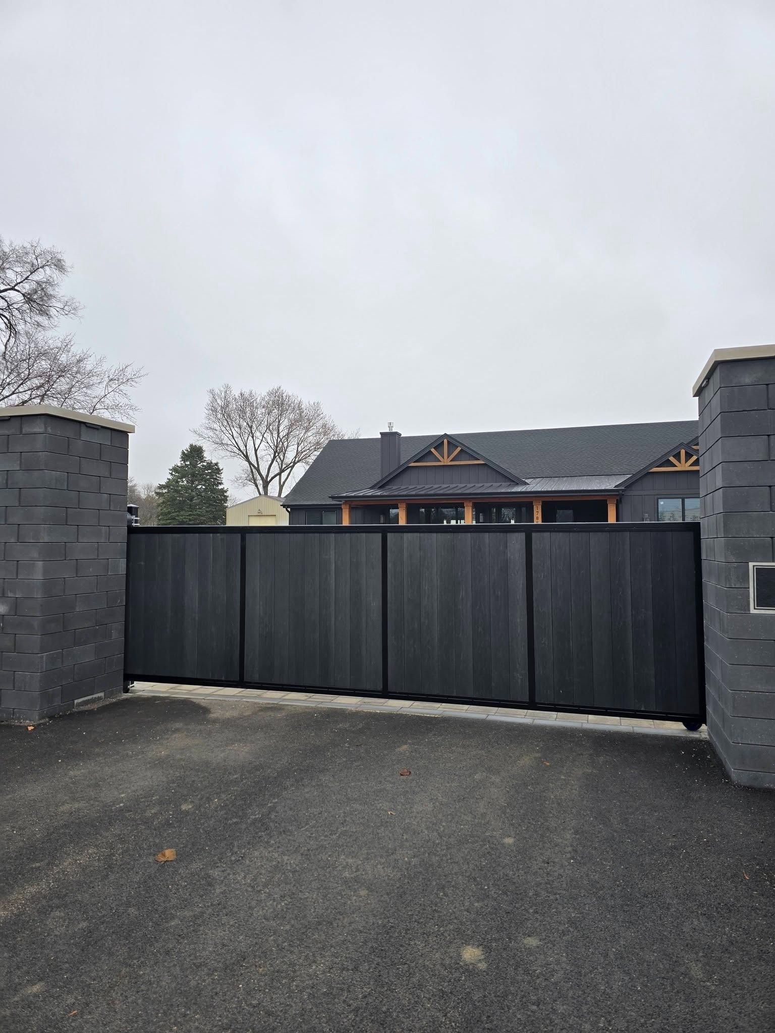 Closed black driveway gate in front of a house on an overcast day