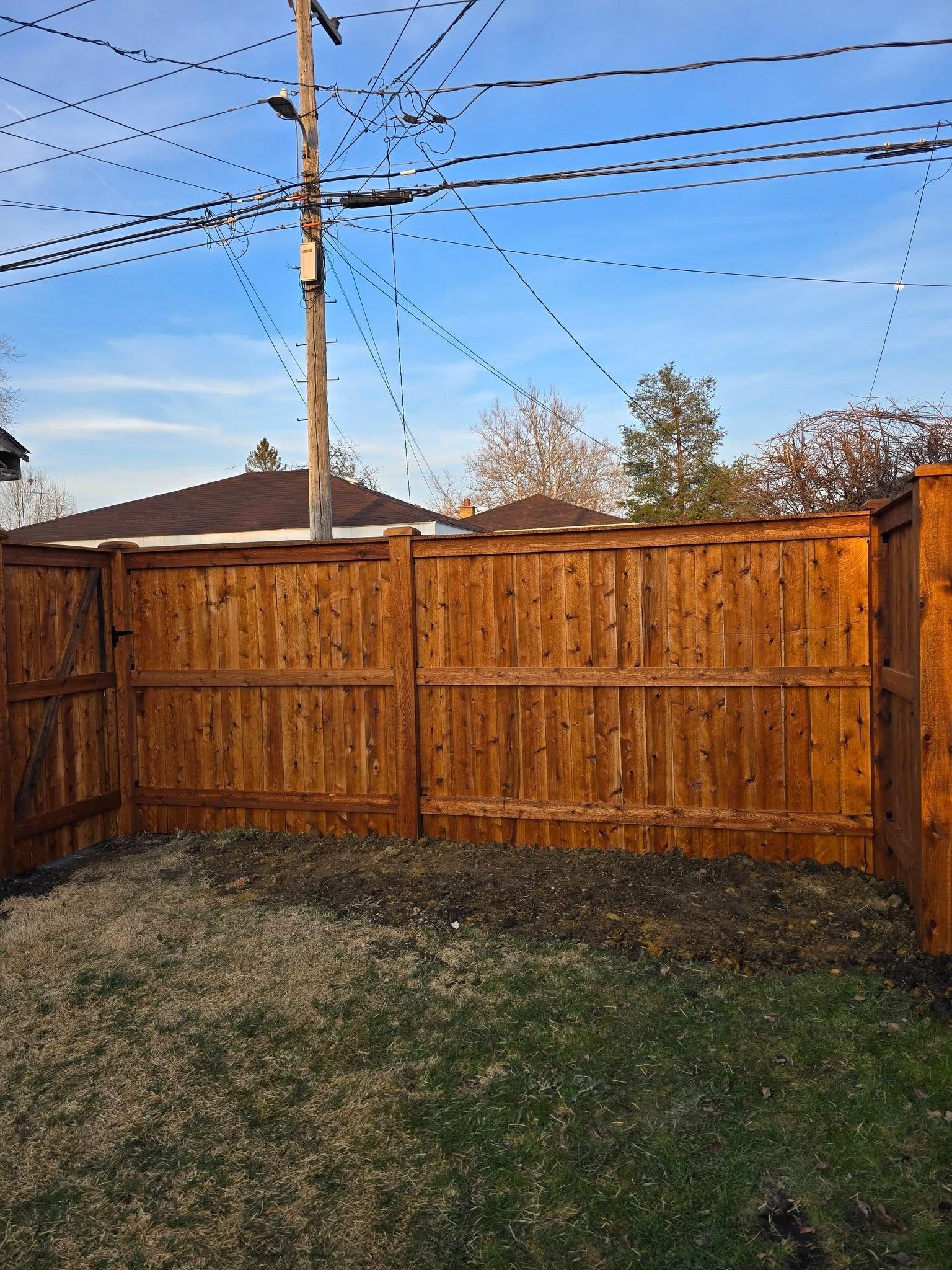 Wooden backyard fence with utility pole and overhead wires under a blue sky, grass in foreground