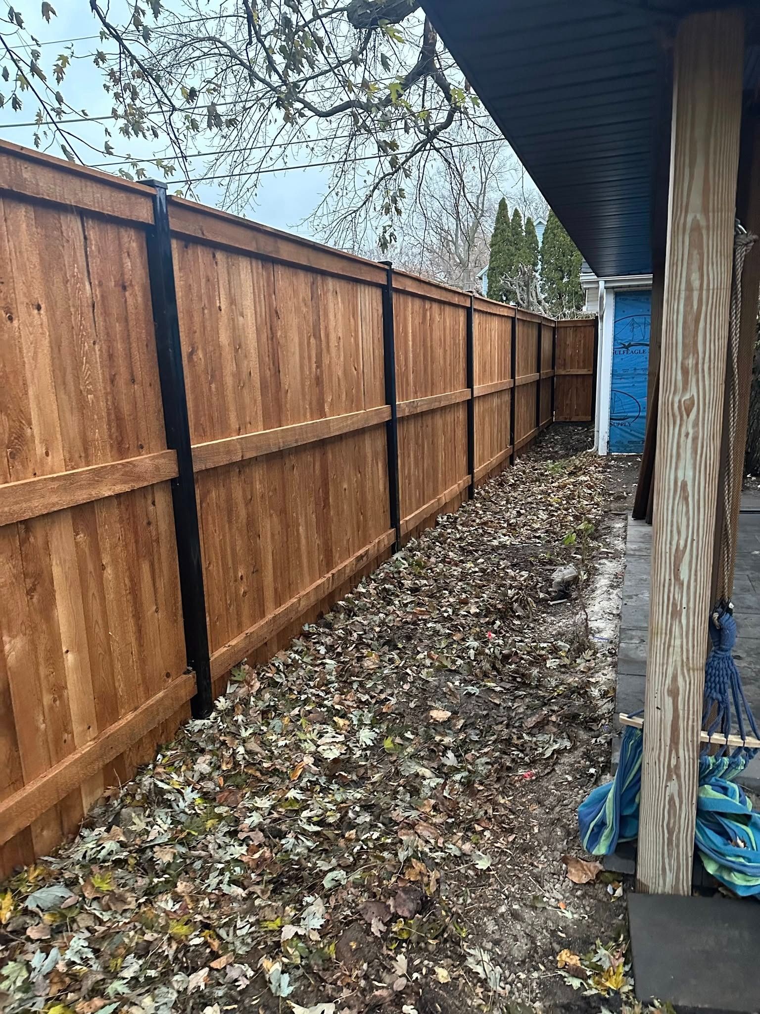 Narrow backyard side yard with wooden fence, gravel ground covered in leaves, and a blue door at the end