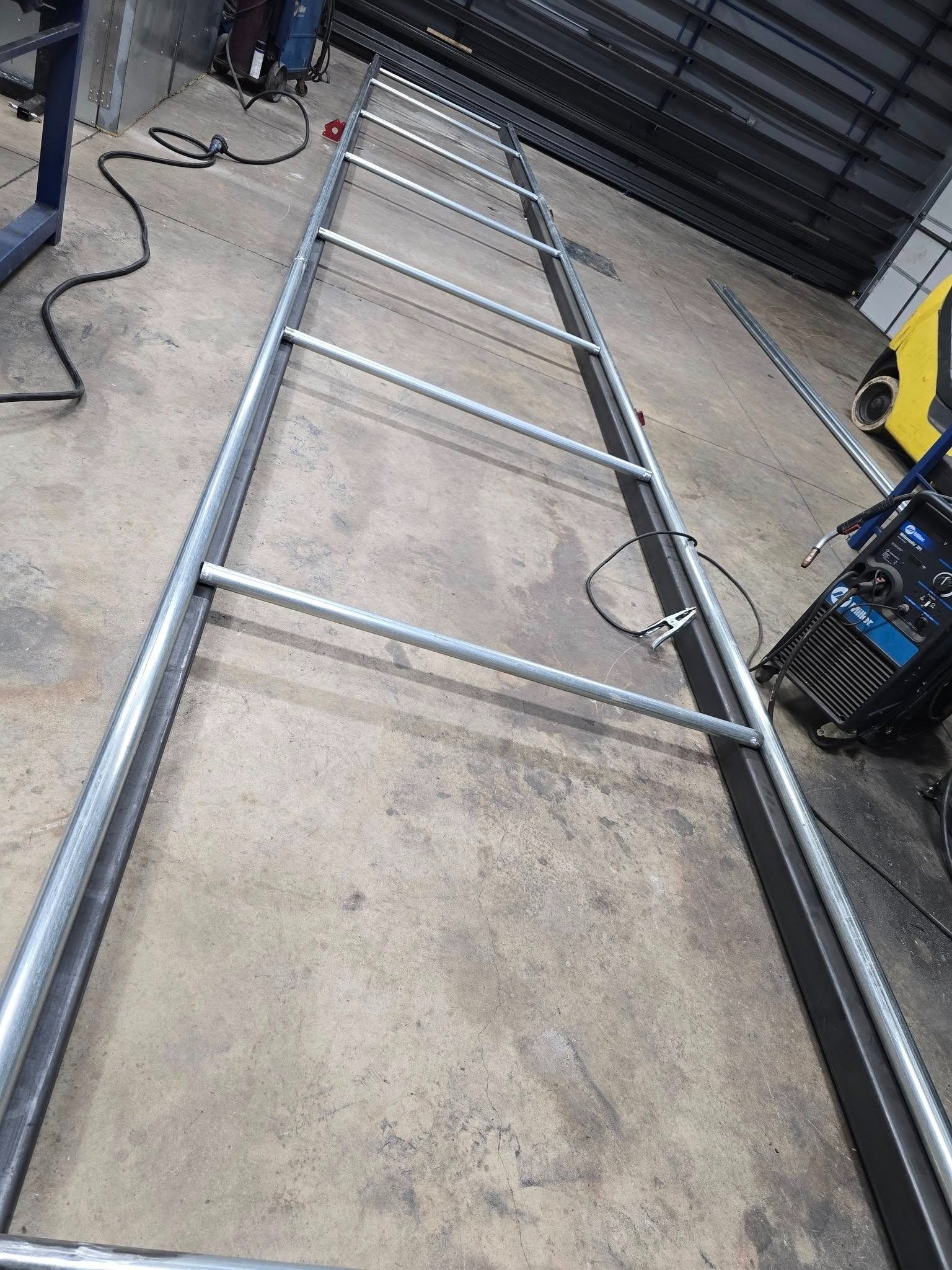 Metal ladder frame lying on a concrete floor in a workshop, with tools and cables nearby.