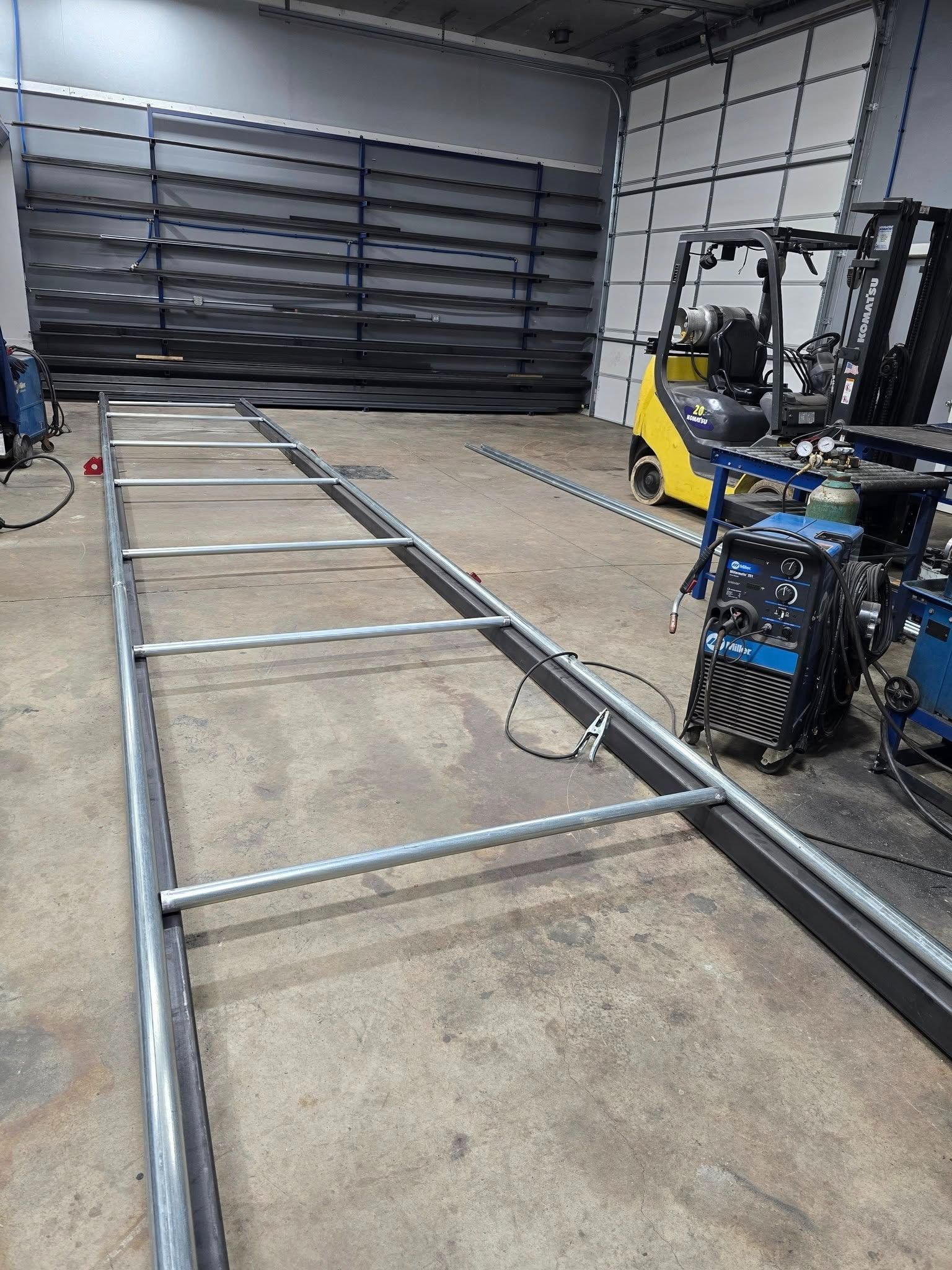 Metal frame sections laid out on a workshop floor beside a forklift in a garage.