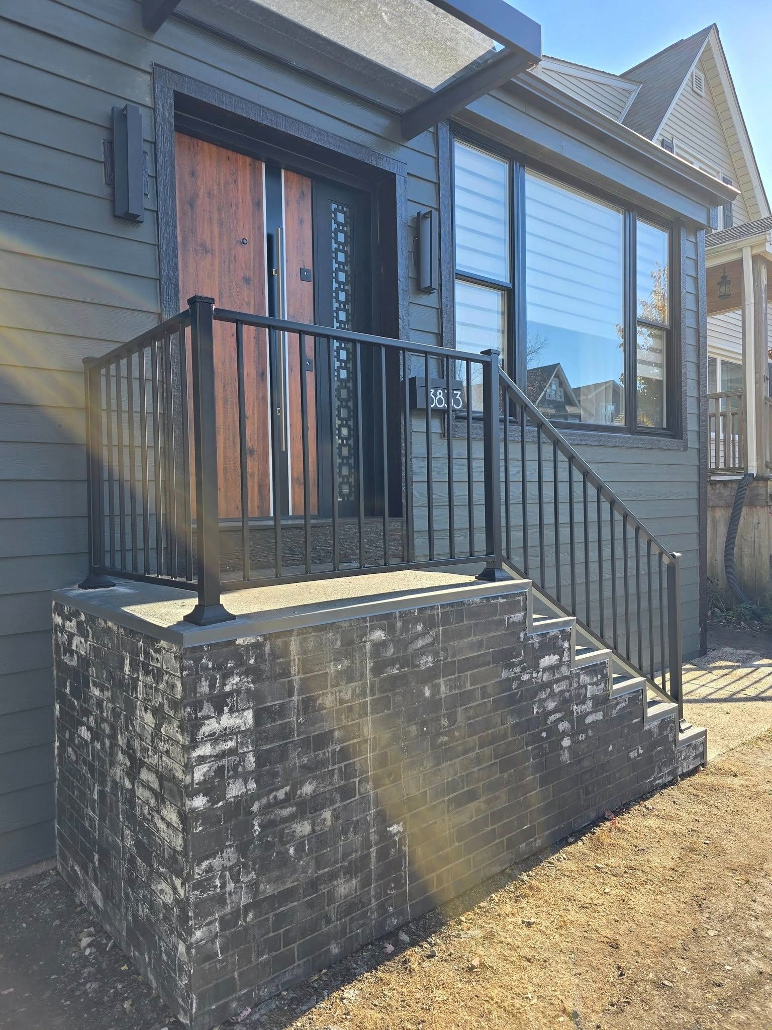 Front porch with black railings, stone steps, and a wooden front door on a gray house.