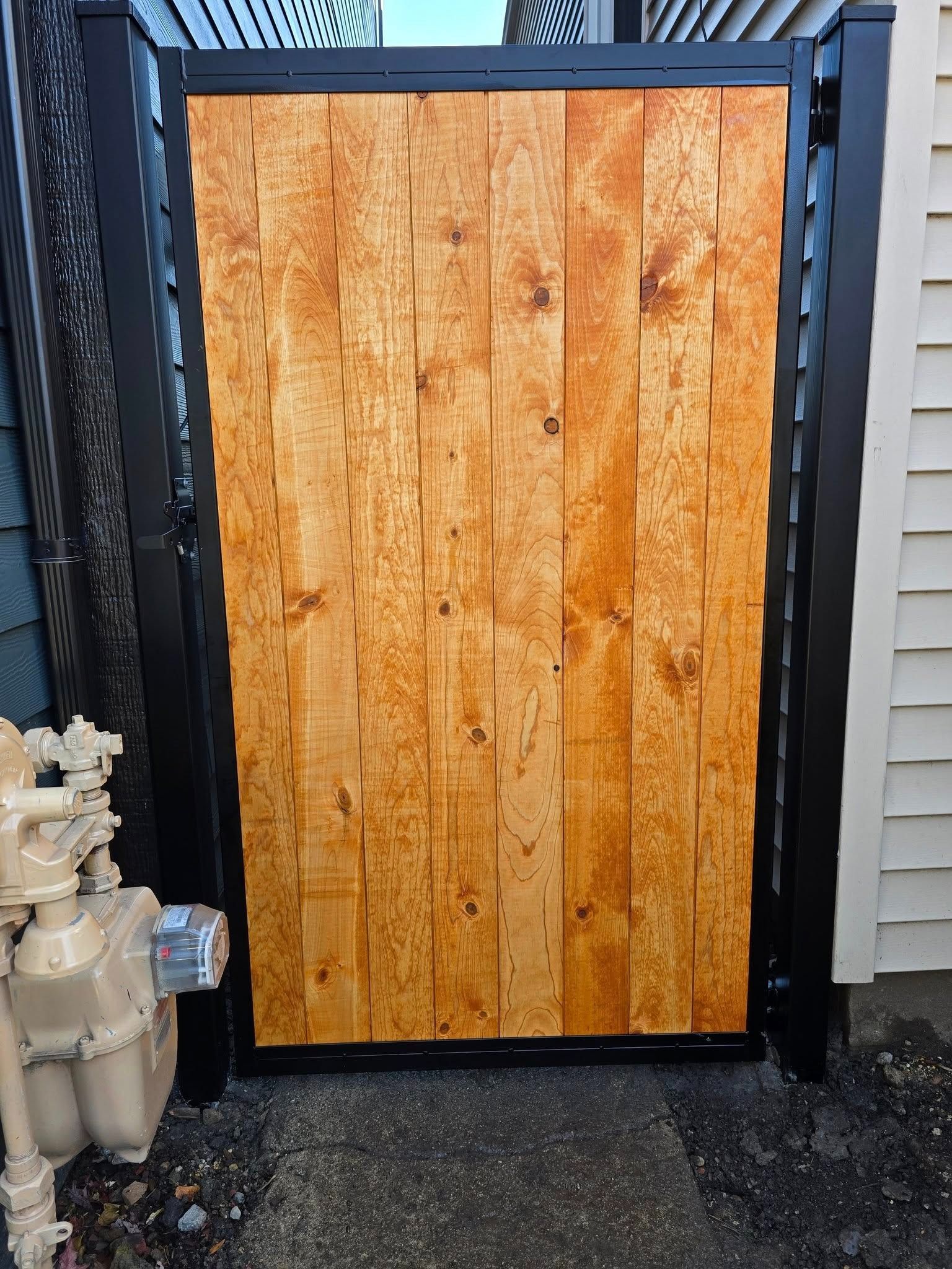 Wooden gate panel with black metal posts beside a white fire hydrant on a gravel path