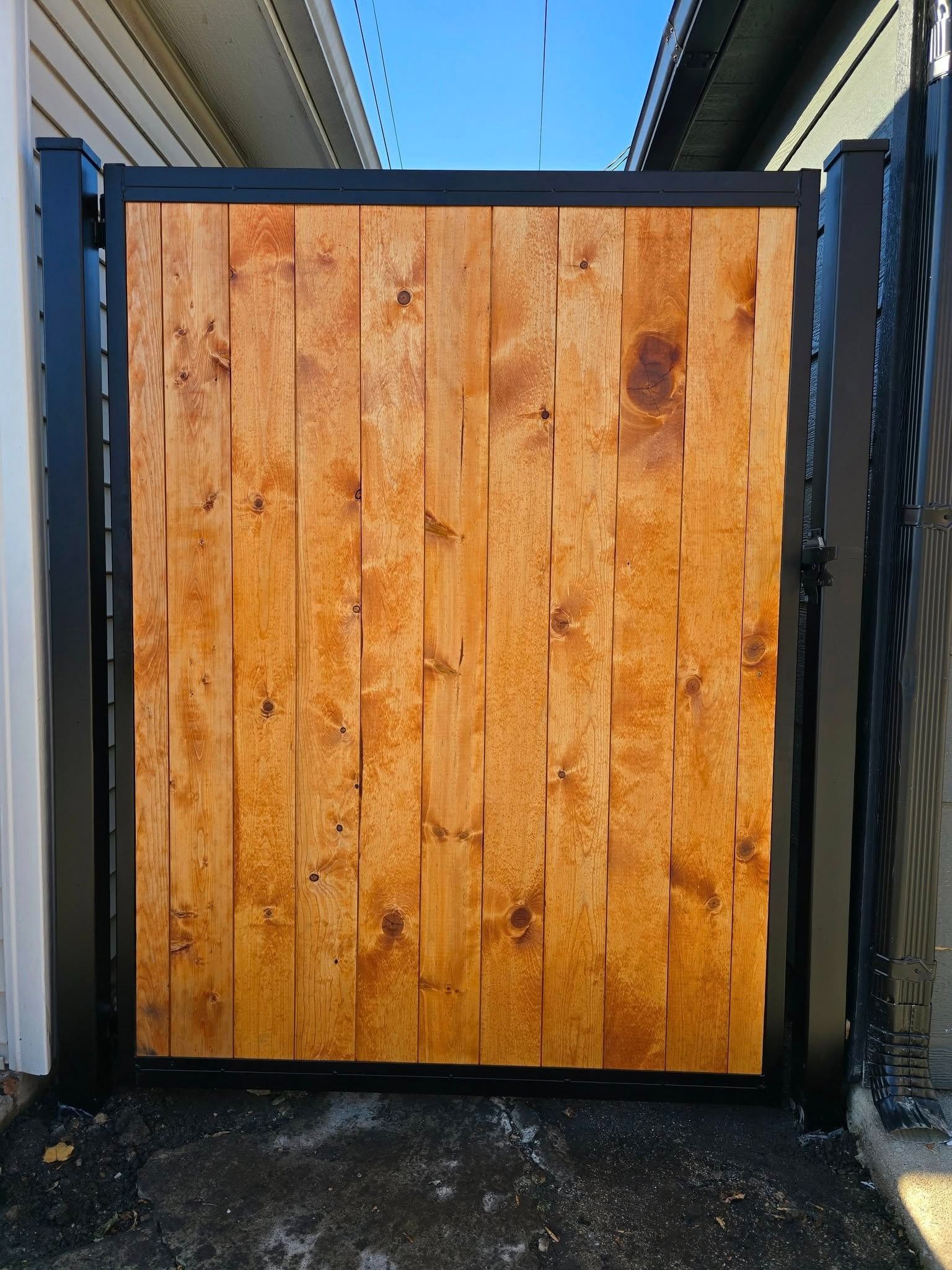 Wooden garden gate with black metal frame between two walls, viewed from the front.